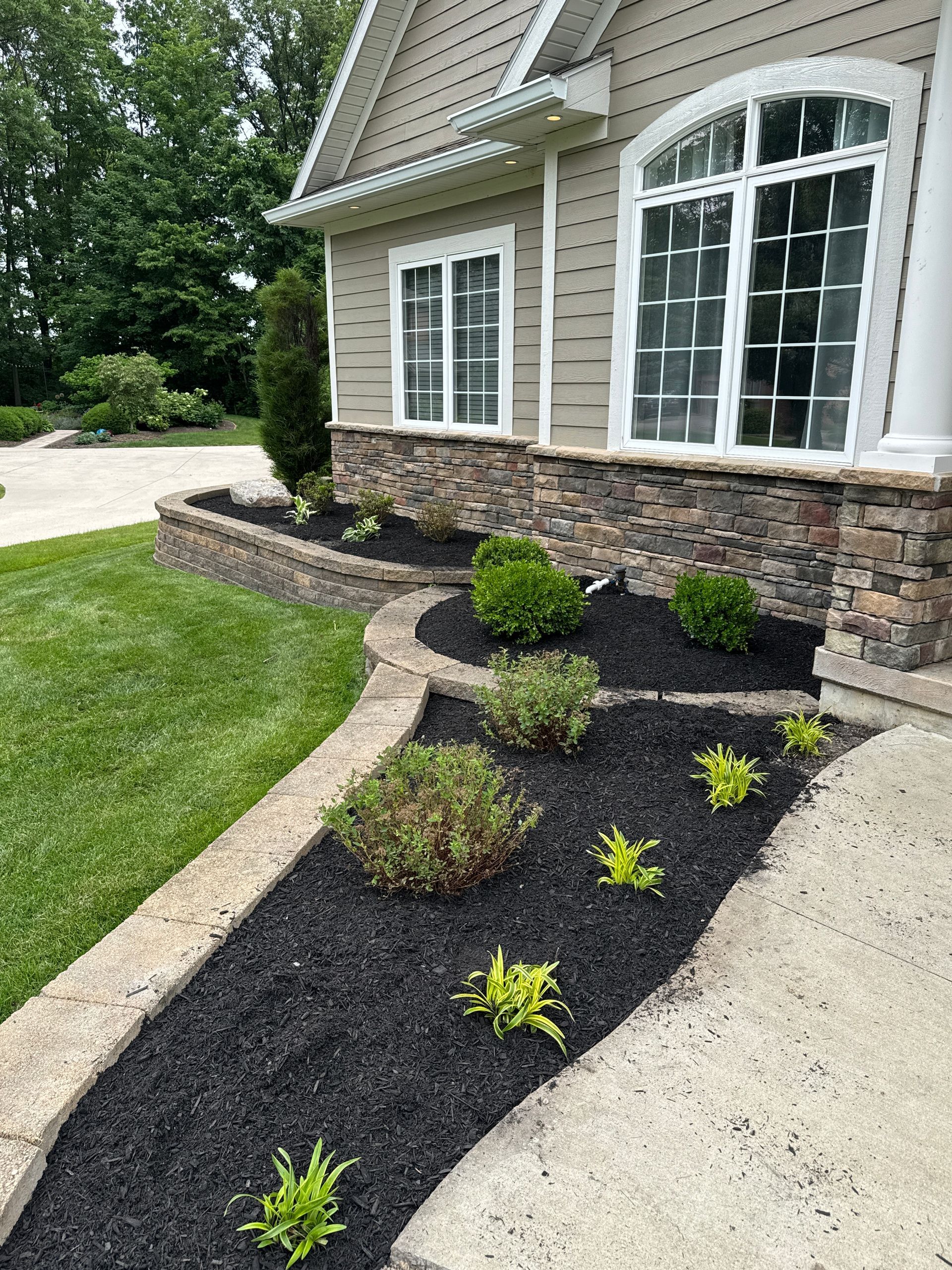 Landscaped front yard with a stone retaining wall and flower beds filled with black mulch.