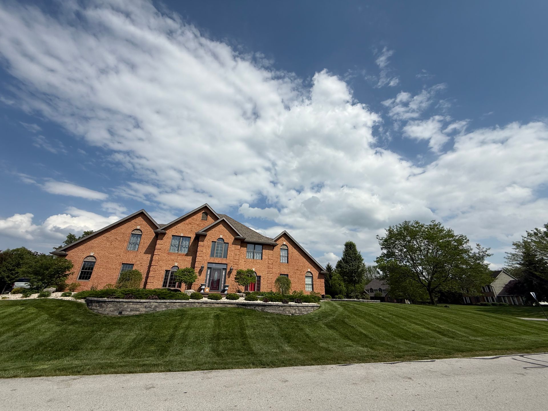 Brick house under a blue sky with puffy white clouds; green lawn in front.