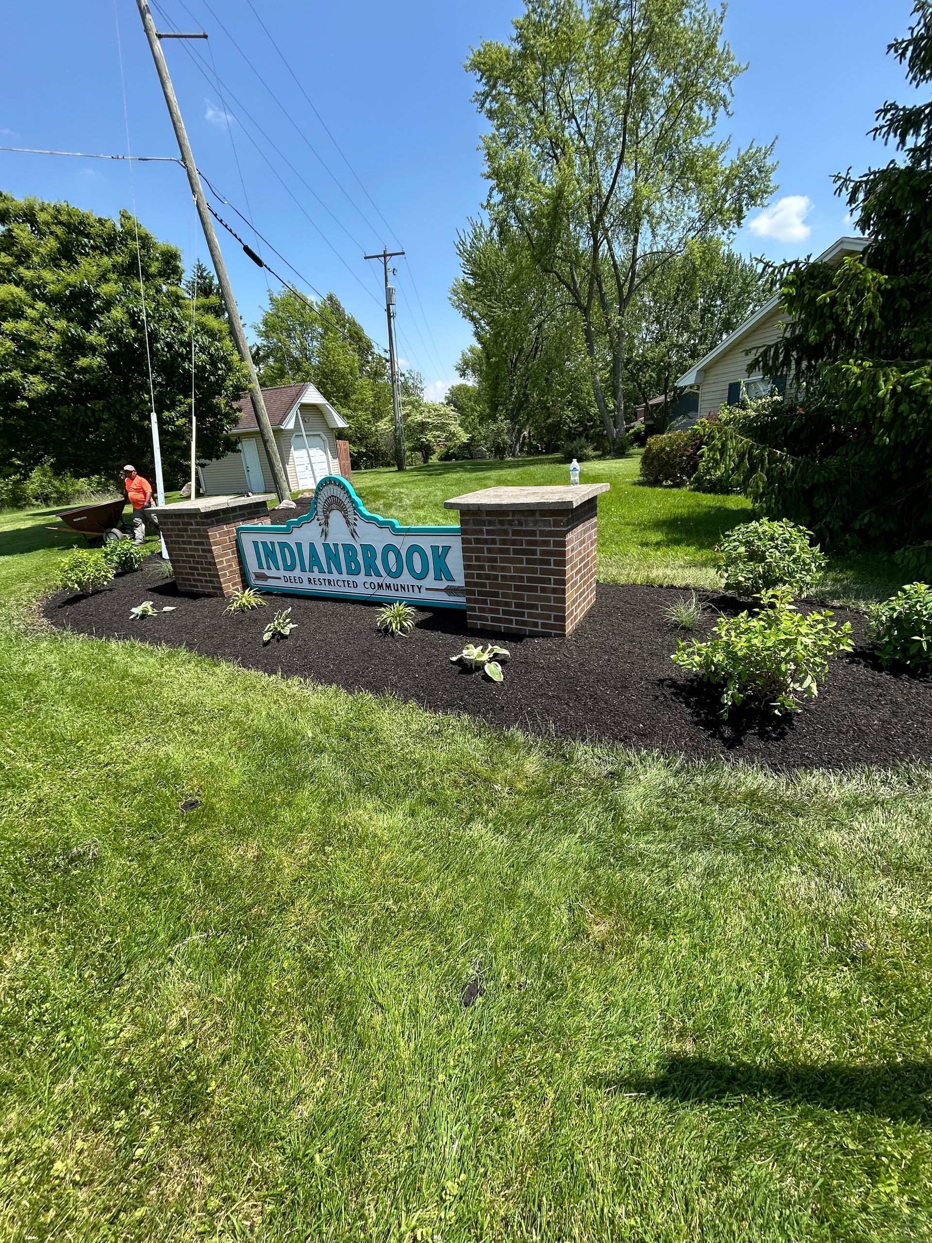 Sign for Holbrook with teal lettering, brick columns, and landscaped flower bed.