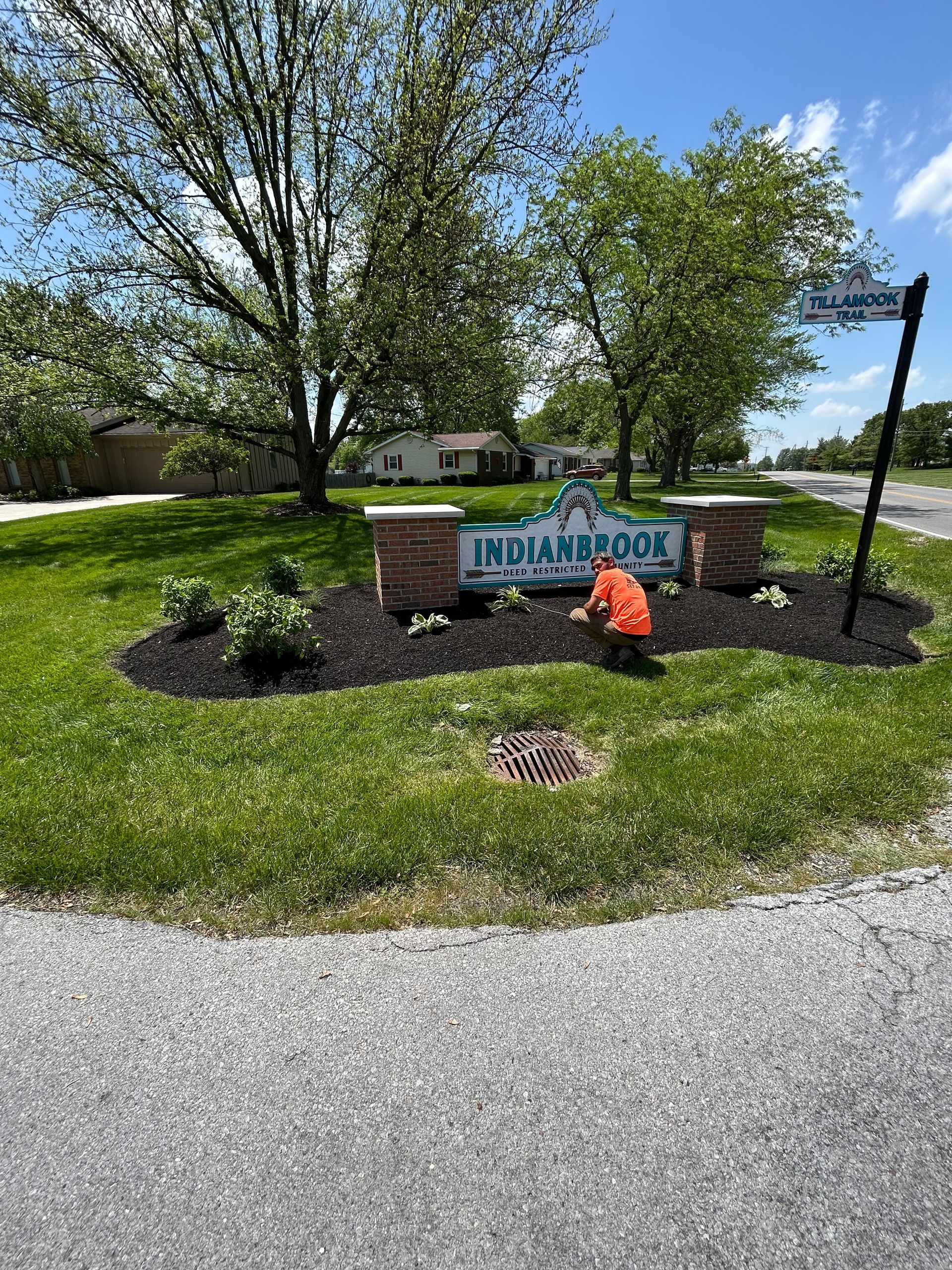 Man working on a flower bed in front of a brick sign that says 