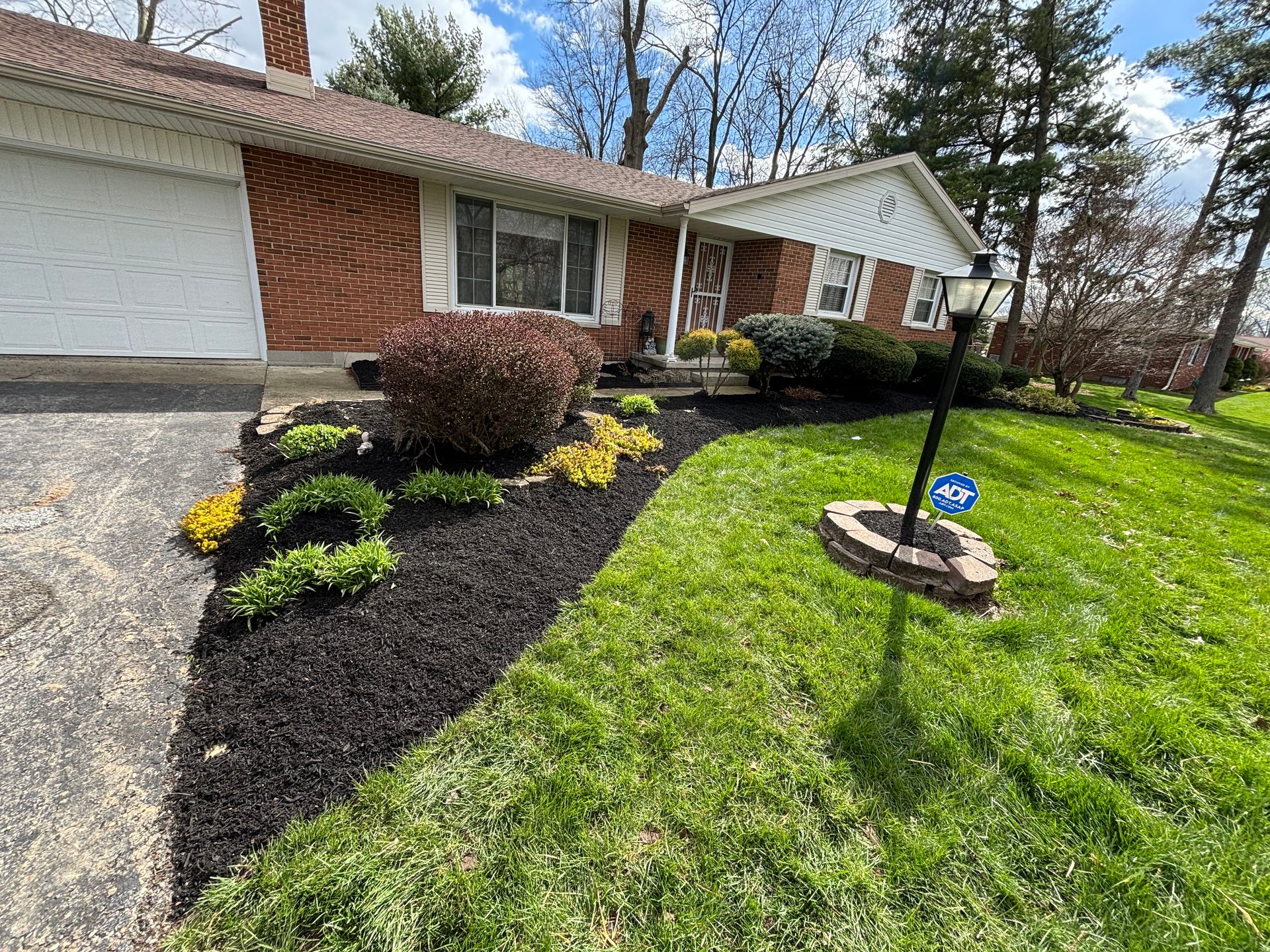 House with landscaping: black mulch, green grass, various plants. A pathway and lamp post in the yard.
