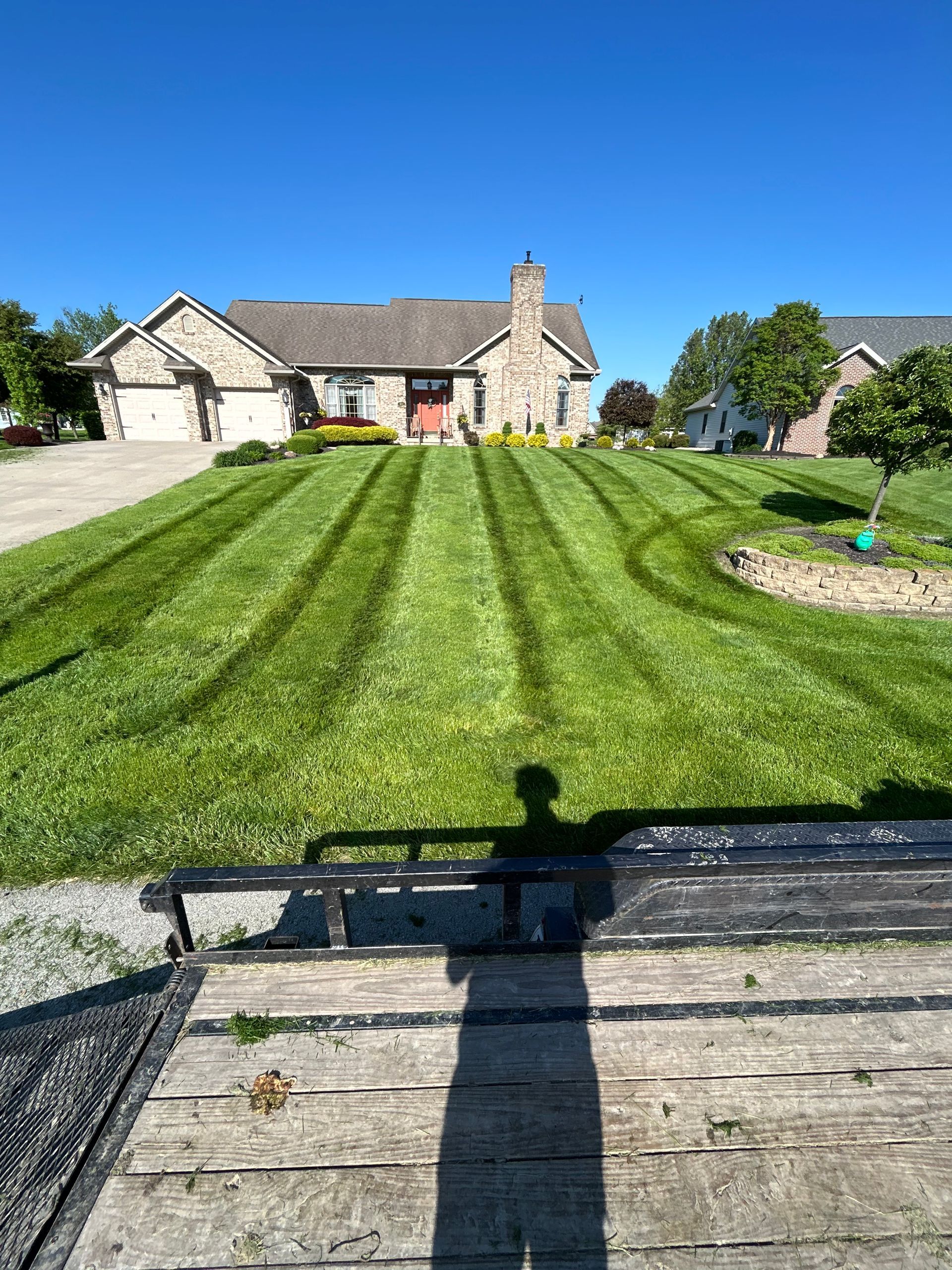 Lawn with distinct mowing patterns in front of a beige house under a clear blue sky.
