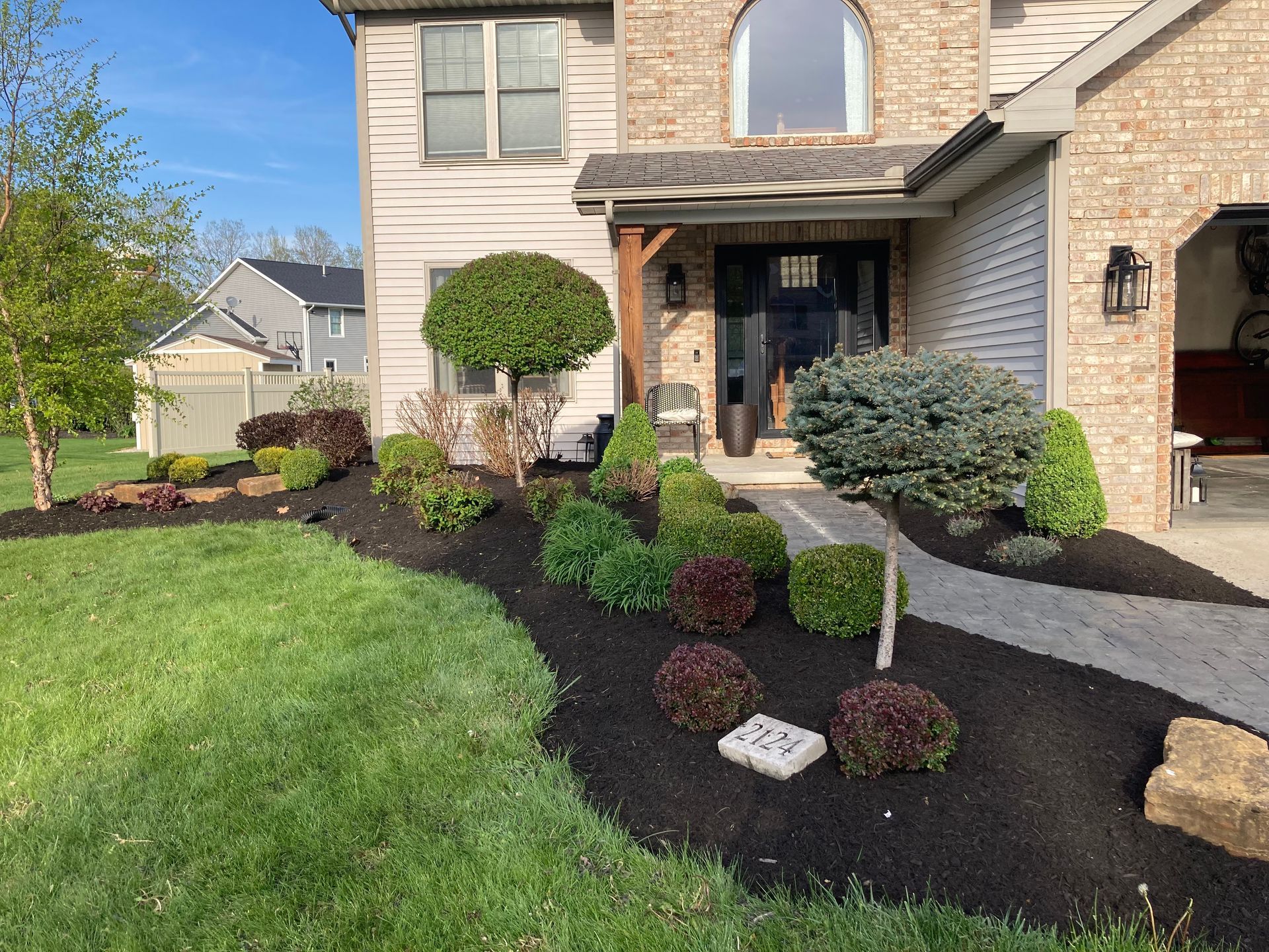 Front yard landscaping with dark mulch, green bushes, and a beige brick house.