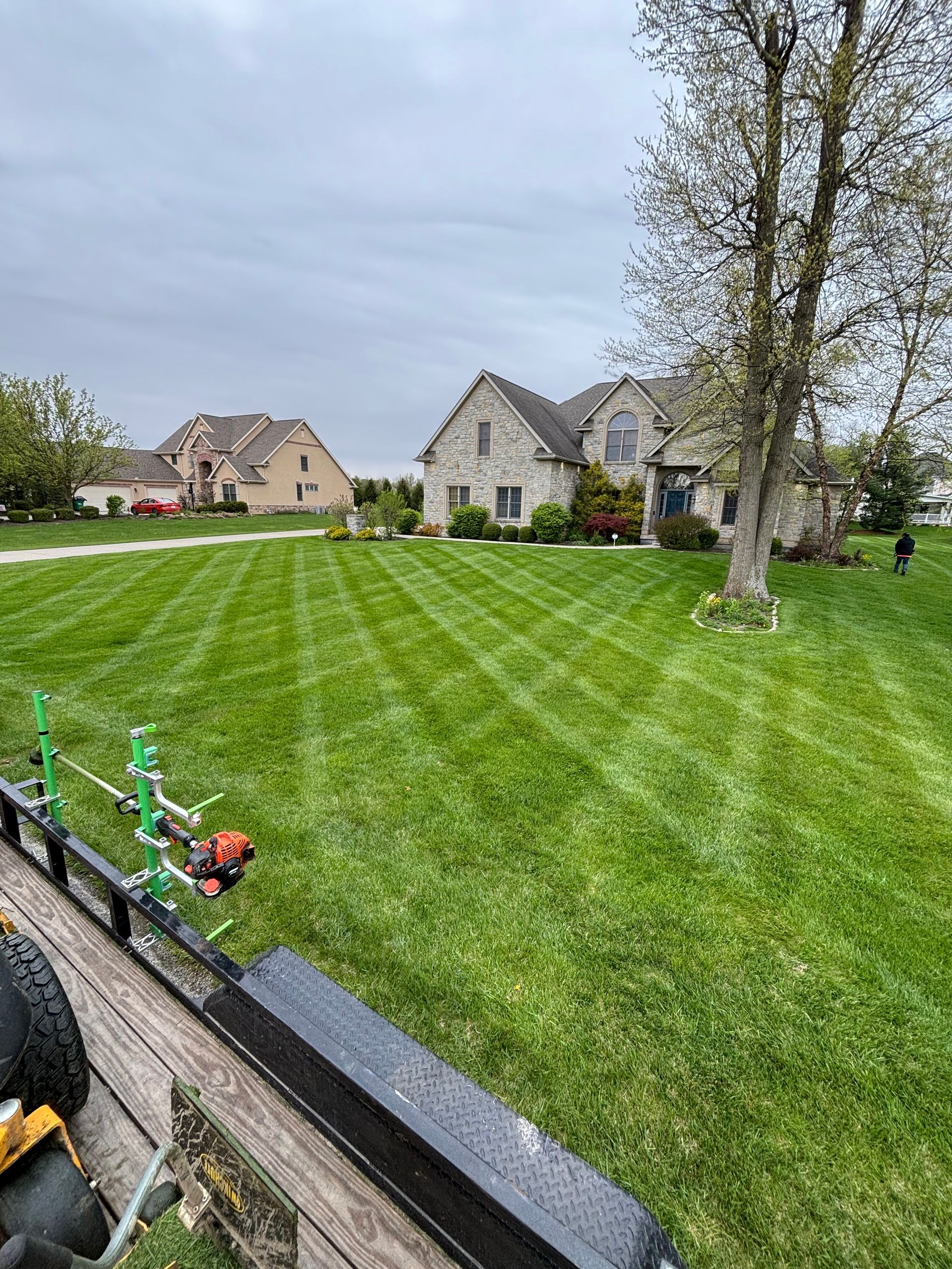 Lawn cut with stripes in front of a stone house on a cloudy day, viewed from the back of a trailer.