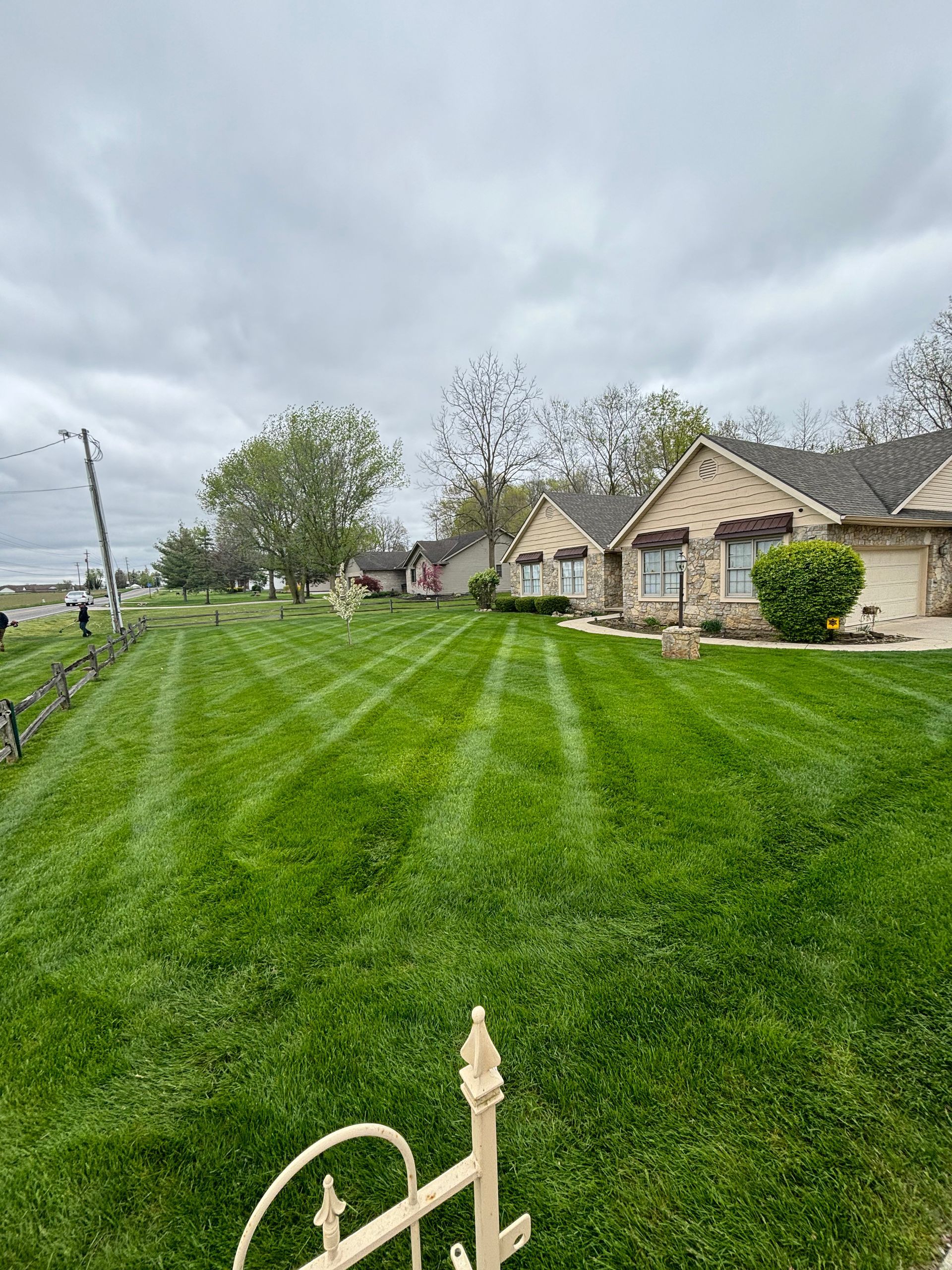 Green lawn with striped mowing pattern in front of brick houses under a cloudy sky.