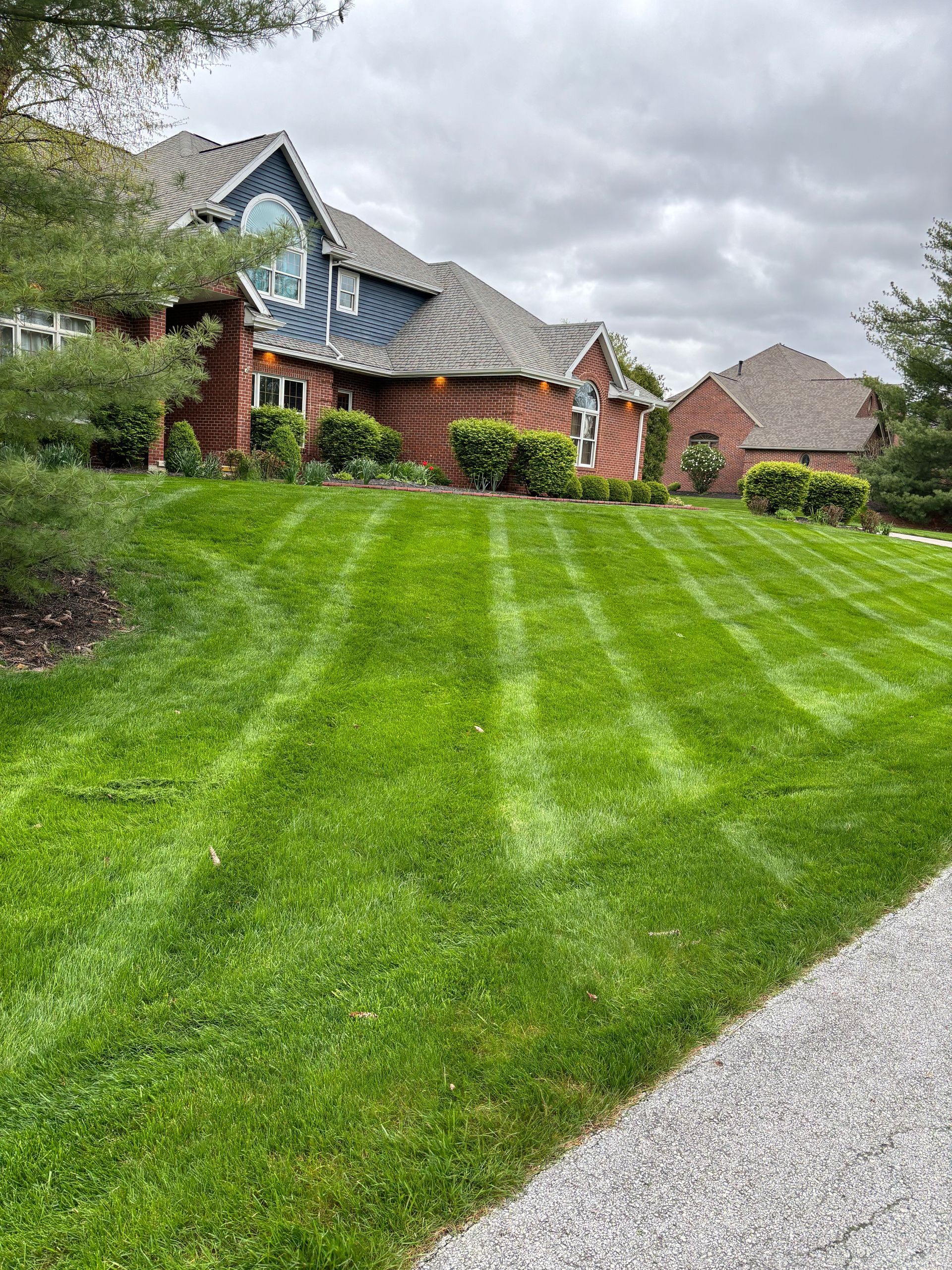 Green lawn with striped mowing pattern in front of a red brick house with blue roof on an overcast day.