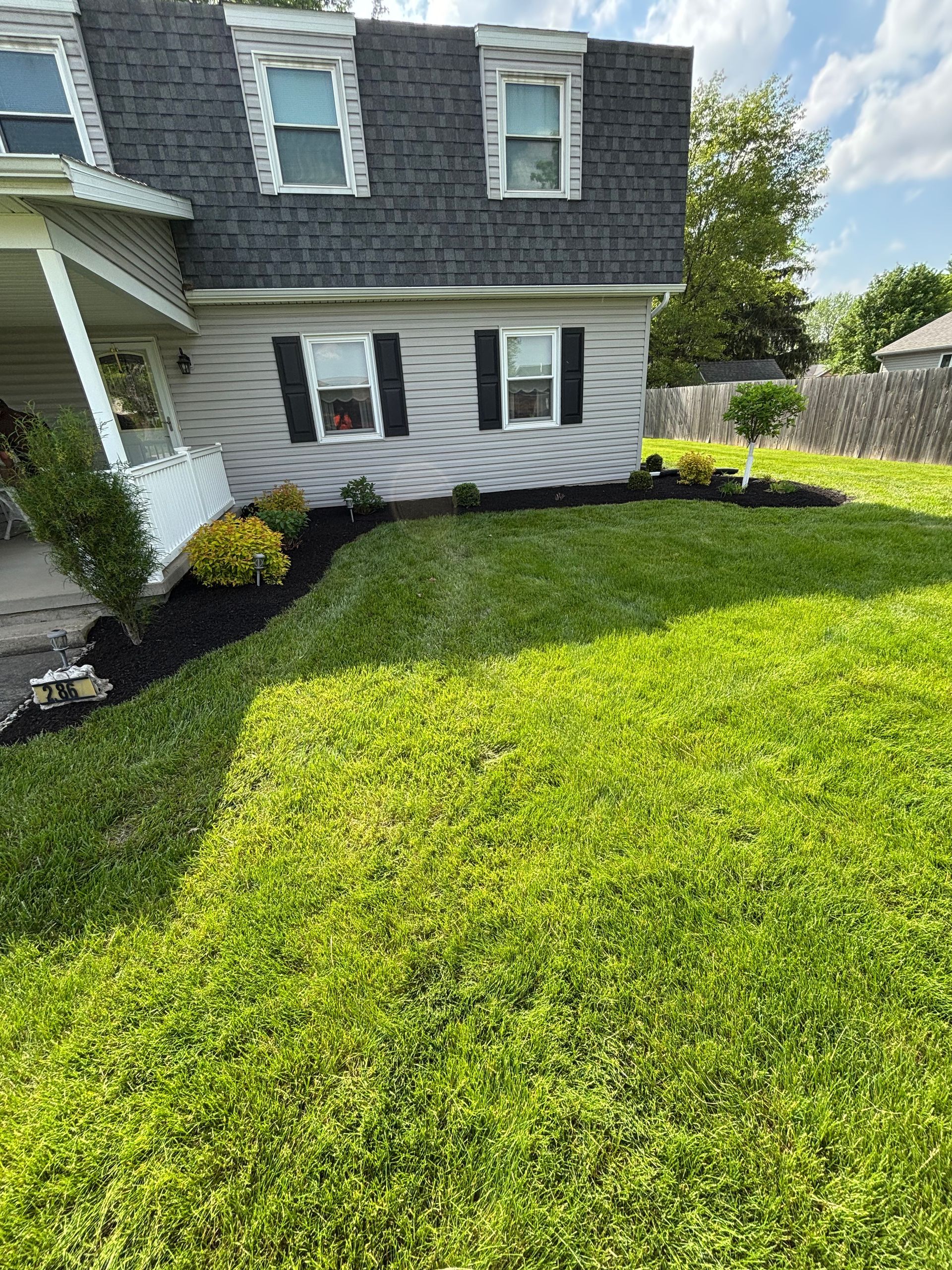 House with gray siding, dark roof, black shutters, fresh mulch, green lawn, blue sky.