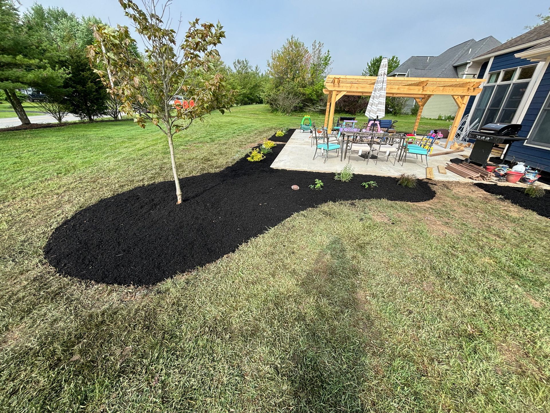 Backyard with a patio, pergola, and freshly mulched flower beds surrounding a tree.