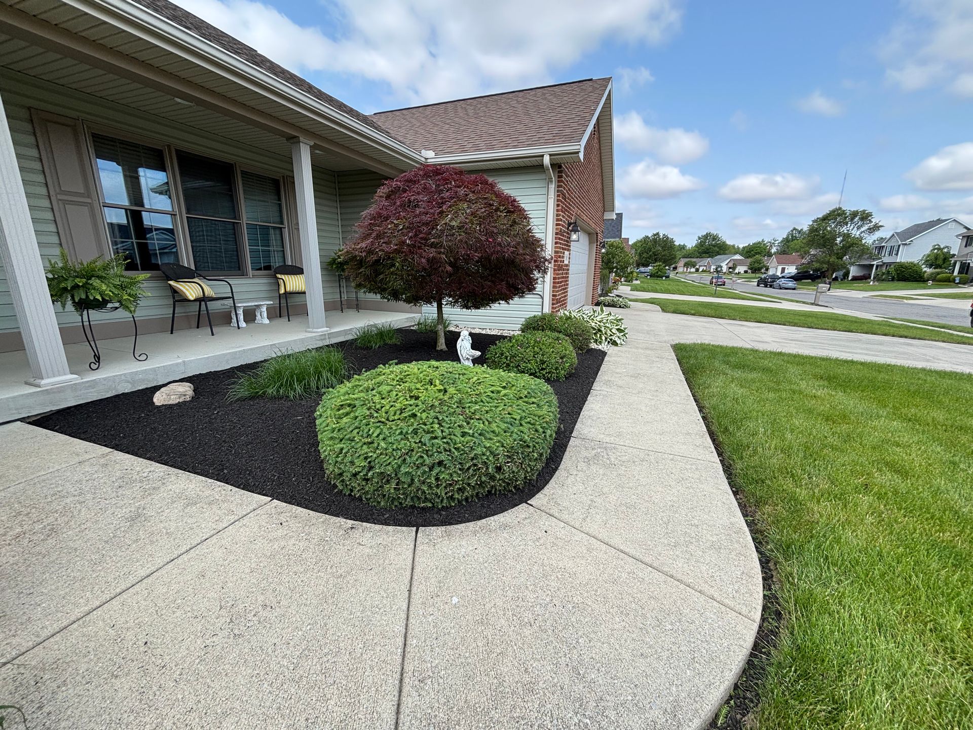 A house with a landscaped front yard and a curved concrete walkway on a sunny day.