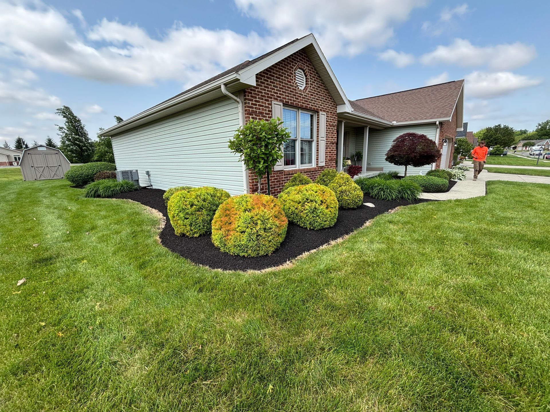 House with lawn and flowerbeds, manicured landscaping, black mulch, green grass and a cloudy sky.