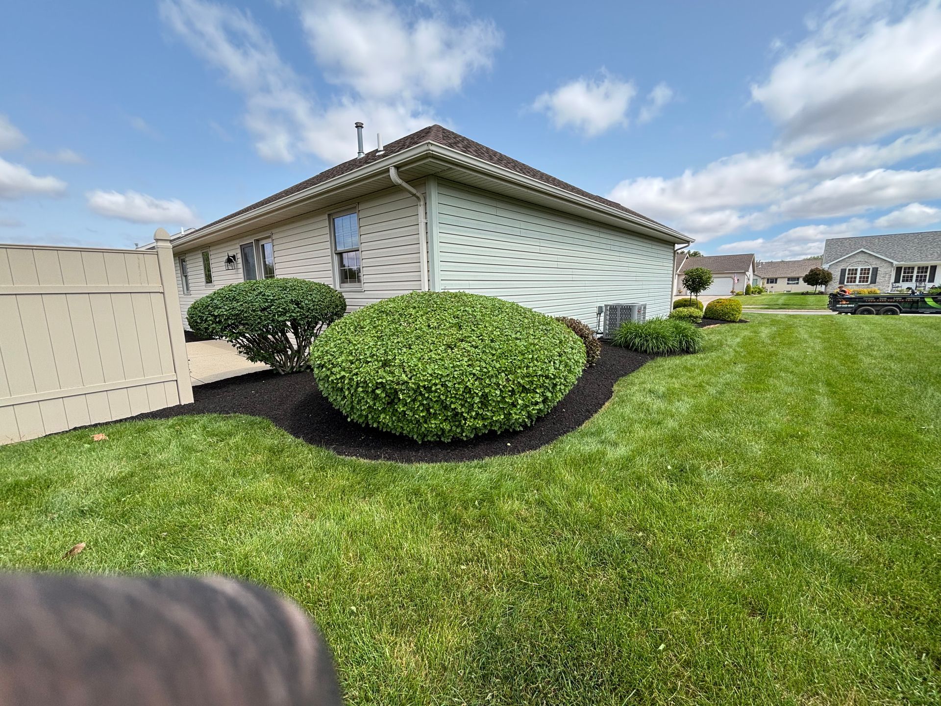 A well-manicured lawn with a beige house and trimmed green bushes surrounded by dark mulch.