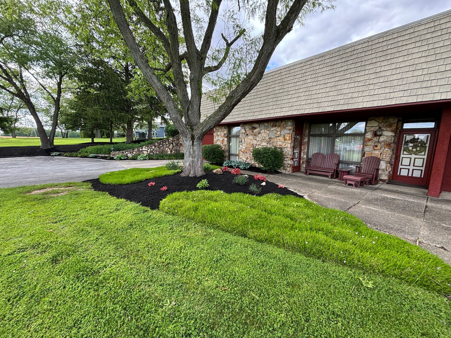 Exterior of a building with a dark mulch flower bed and green grass; a large tree is in front.