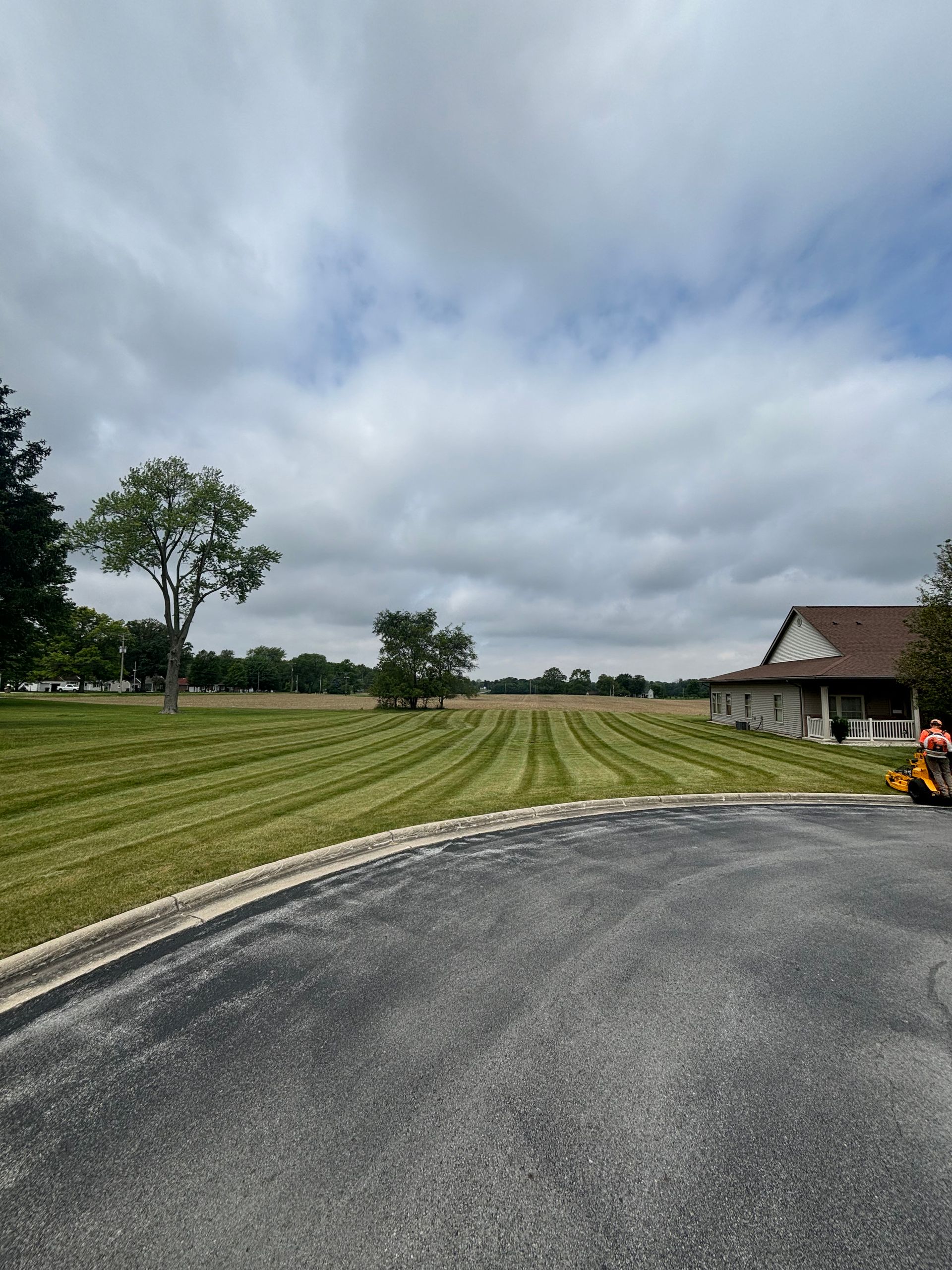 Large field of freshly mowed green grass under a cloudy sky, next to a house and driveway.