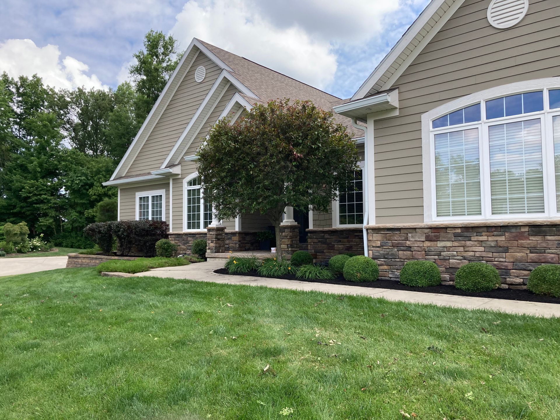 Beige house with stone facade, arched window, lush green lawn, and a small tree.