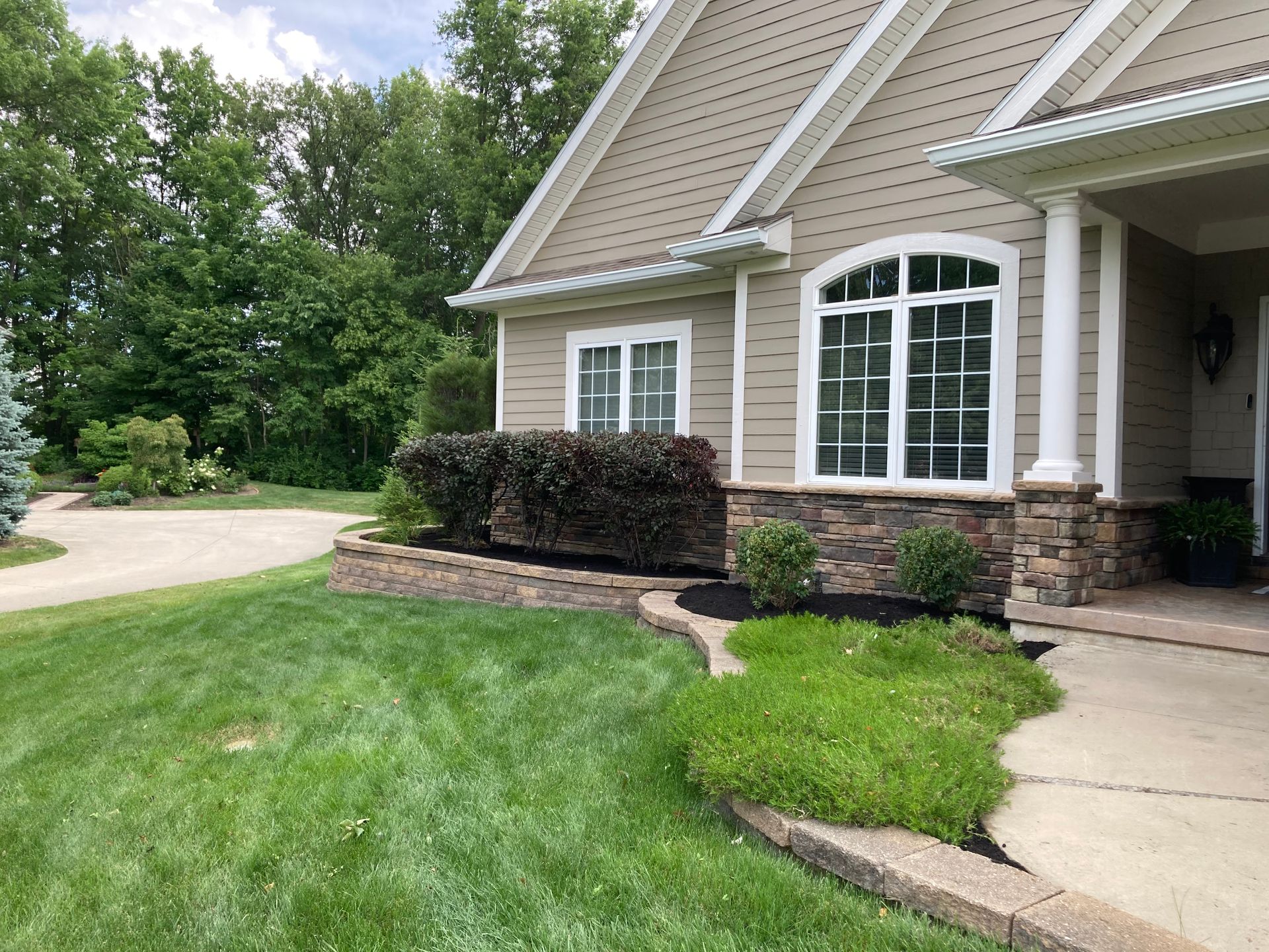 House exterior with tan siding, stone accents, manicured lawn, and landscaping.