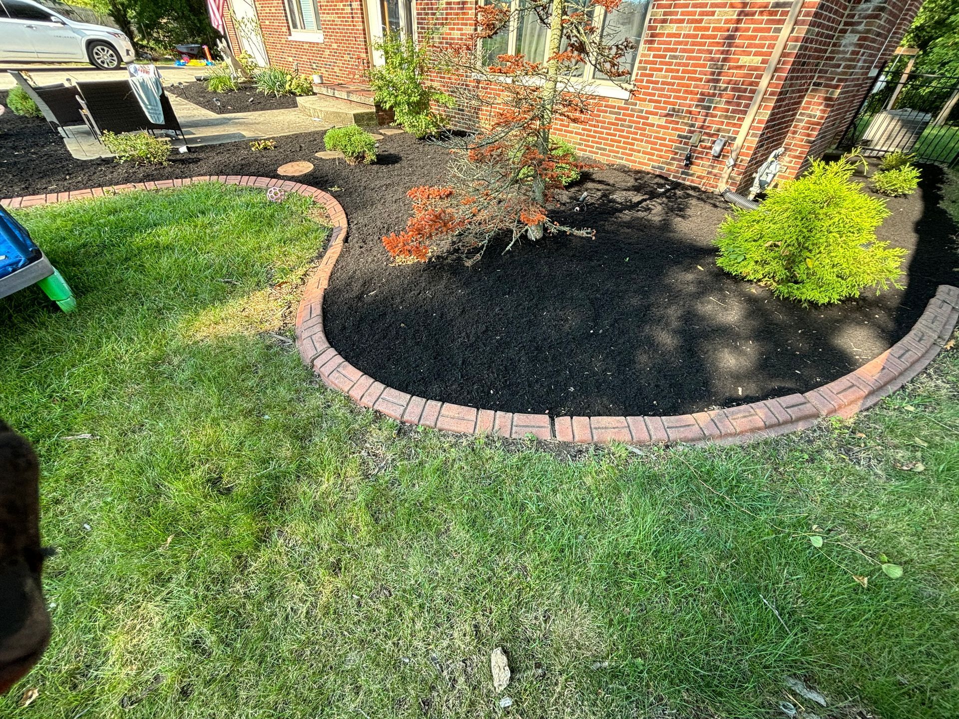 Lawn with brick edging, flower bed, and house with brick siding. Black mulch and green grass.