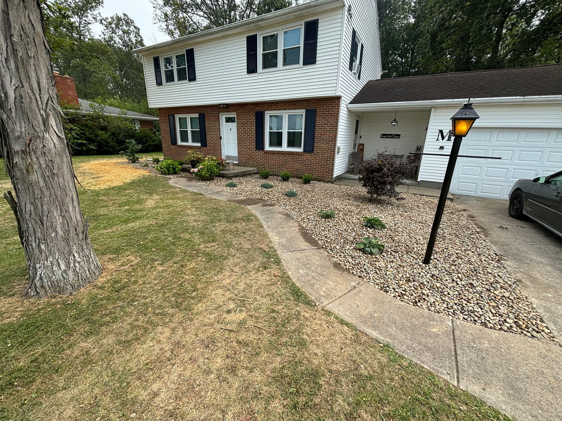 Two-story house with brick and white siding, rock landscaping, and a walkway leading to the front door.