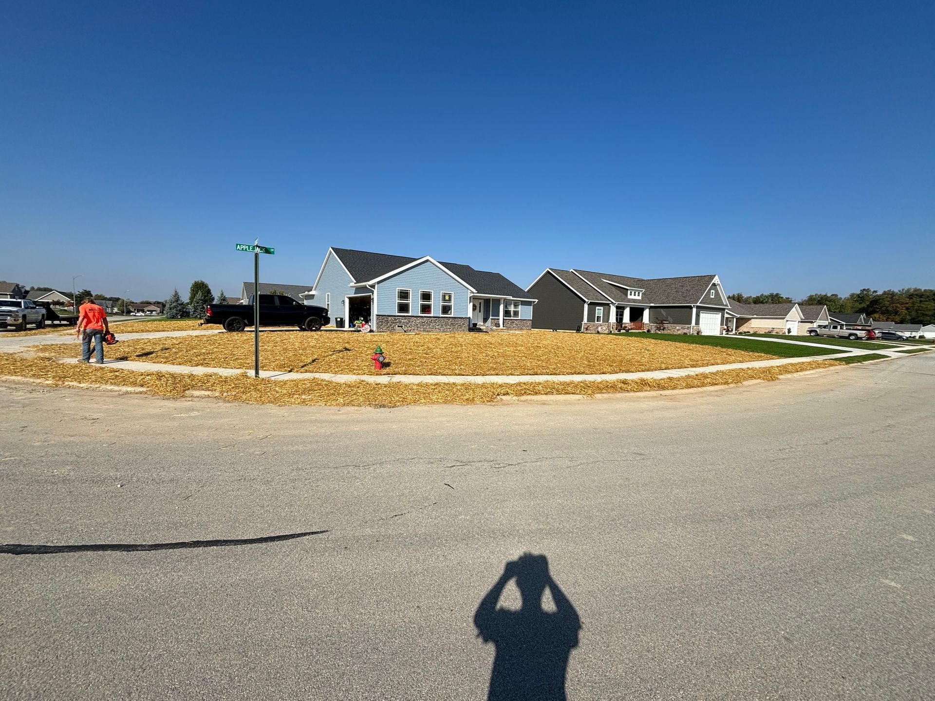 A sunny day view of newly constructed houses, surrounded by mulch and gravel roads, in a suburban setting.