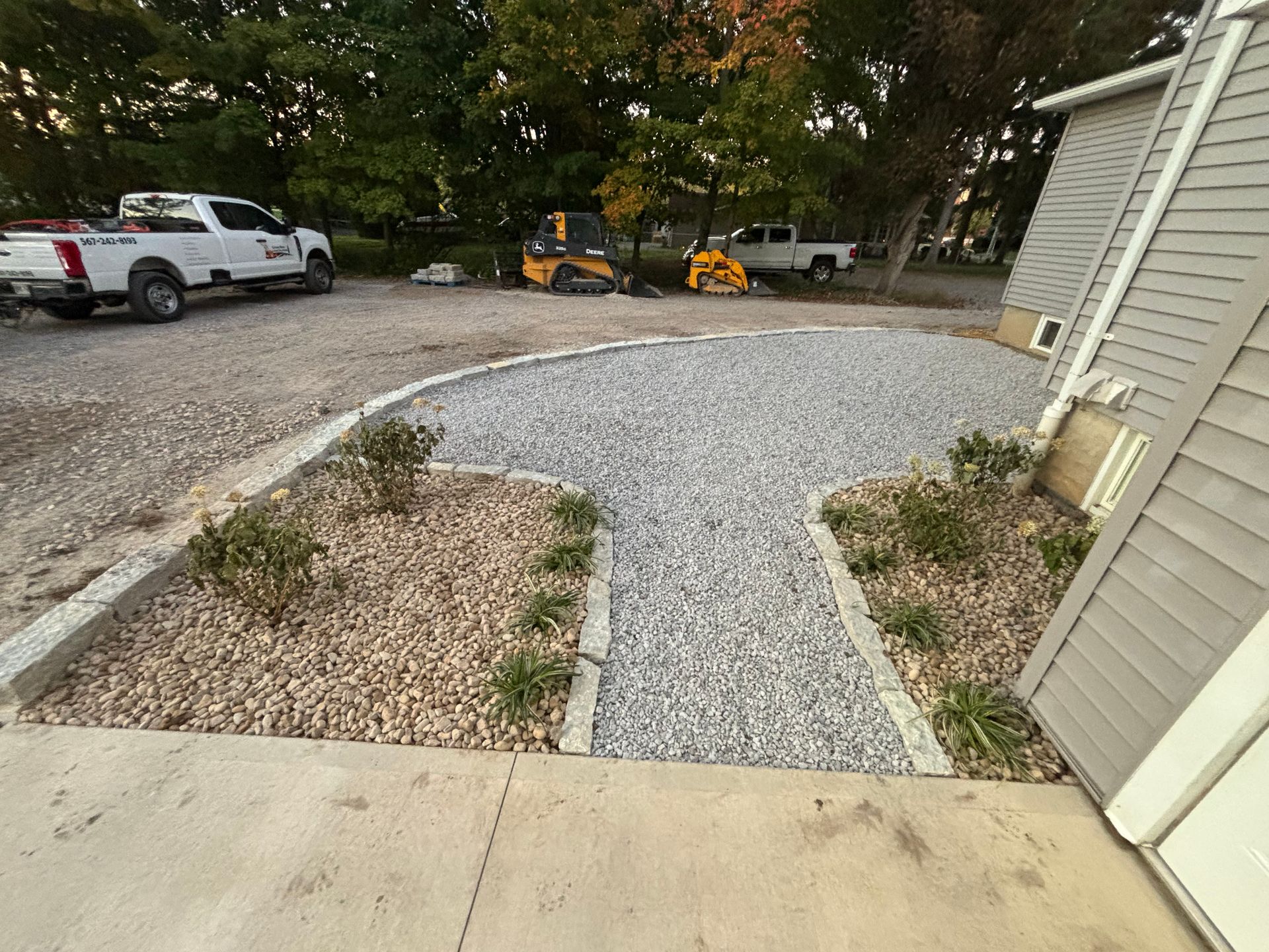 Gravel driveway with stone border, landscaping, and construction vehicles parked behind it.