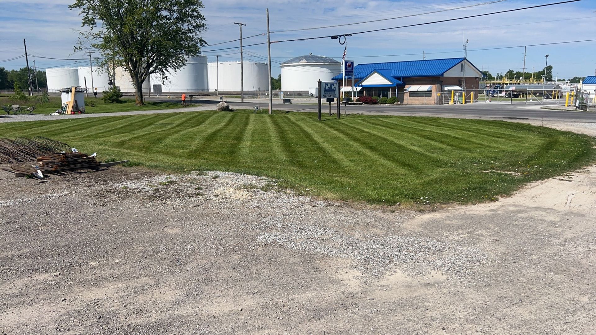Well-manicured grass with industrial buildings in the background under a blue sky.
