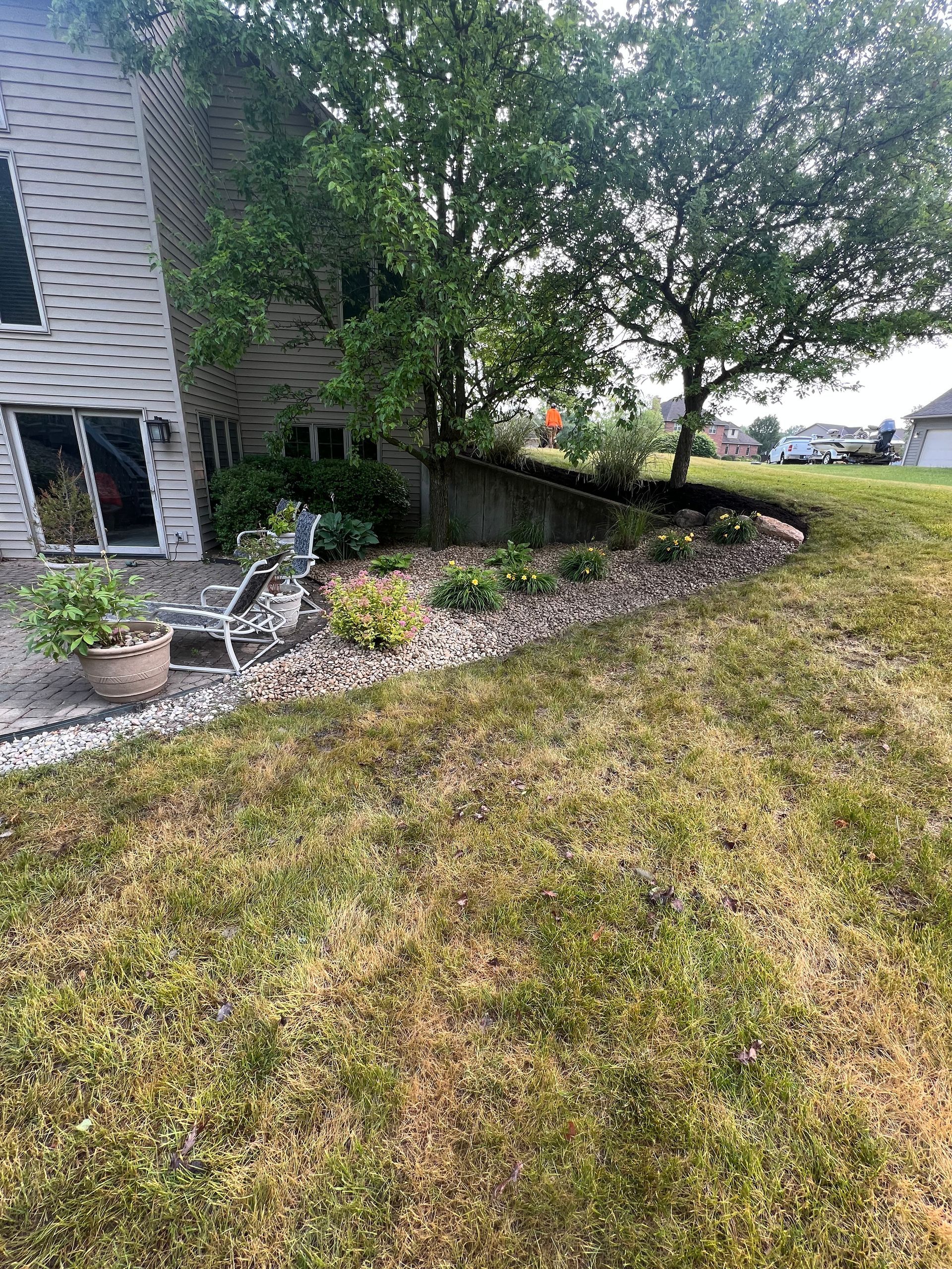Lawn next to a house with a rock-lined flower bed and two chairs on a patio.
