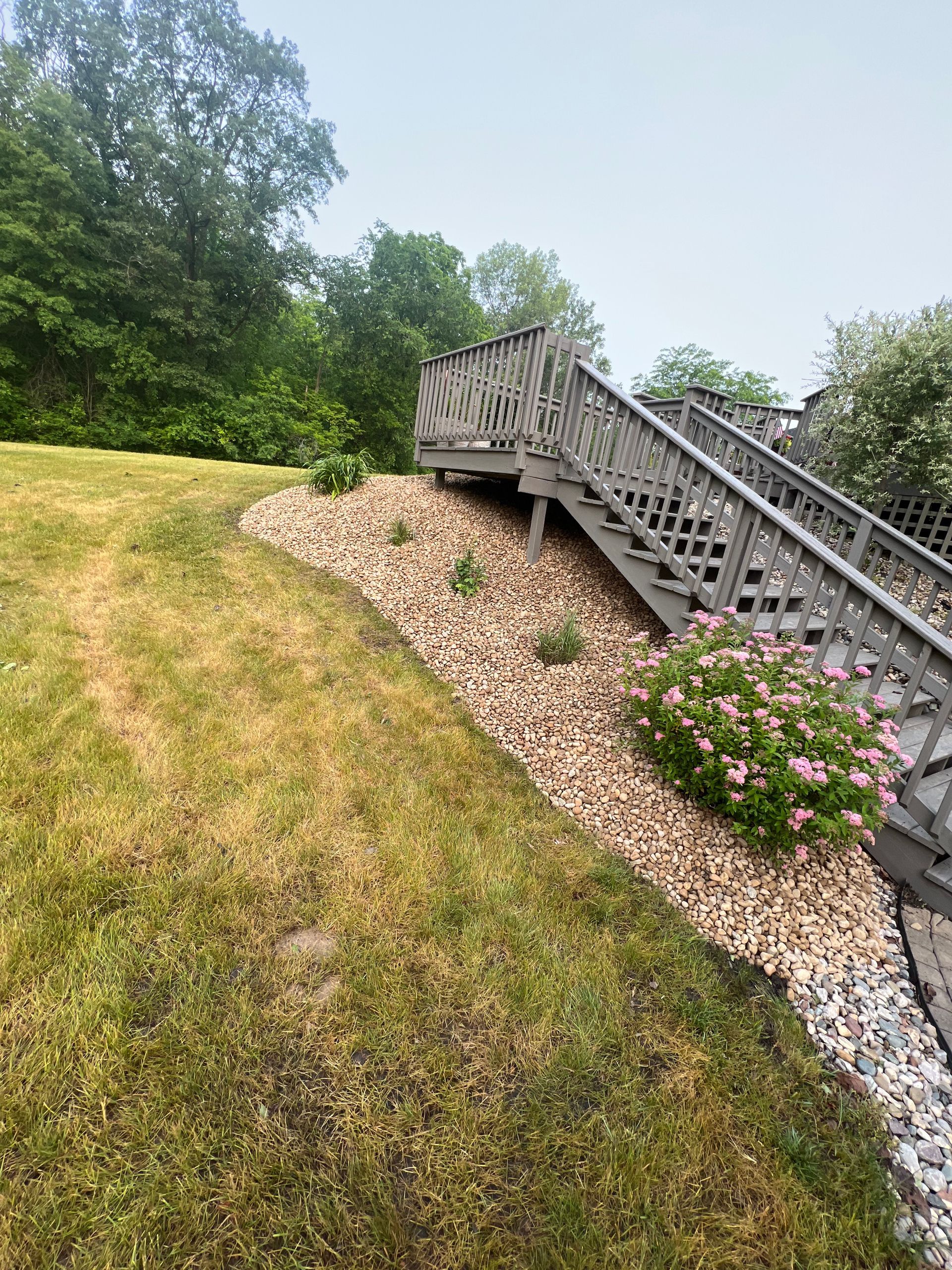 Wooden staircase leading to a deck, surrounded by landscaping on a grassy slope.