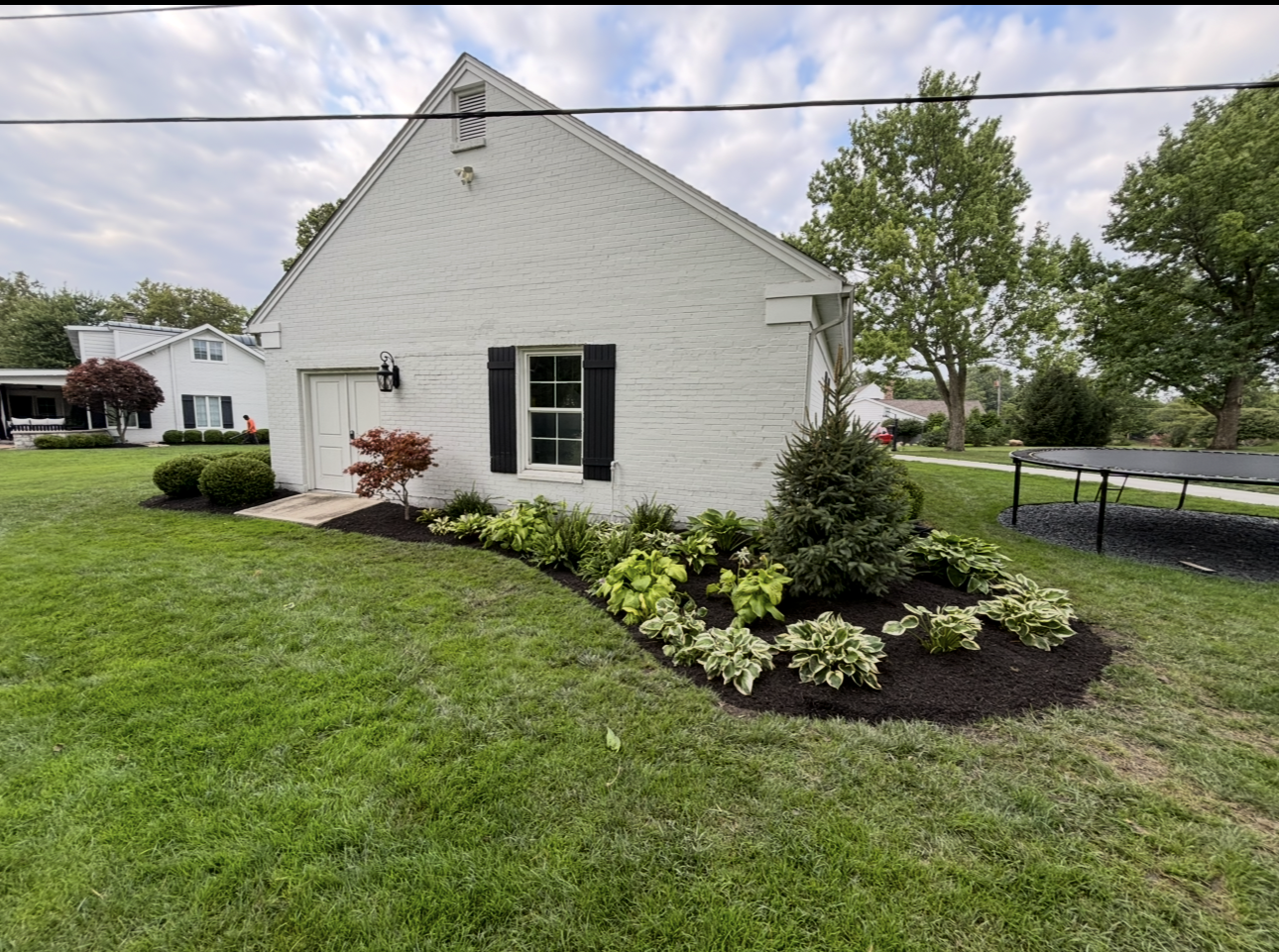 White brick building with flower bed, green grass, and black shutters.