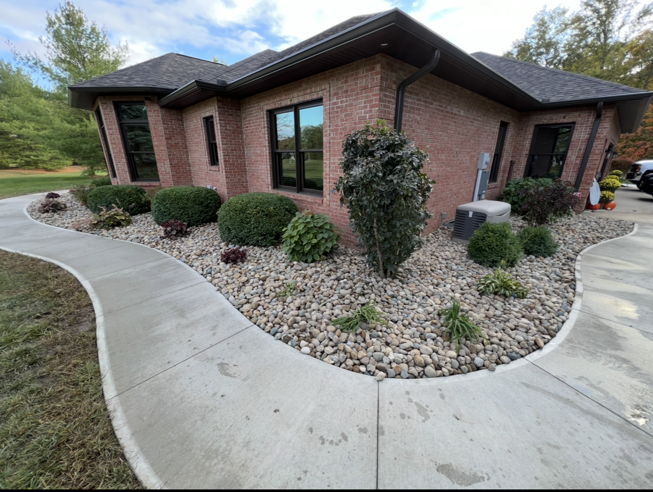 Red brick house with rock landscaping, a curved sidewalk, and green bushes.