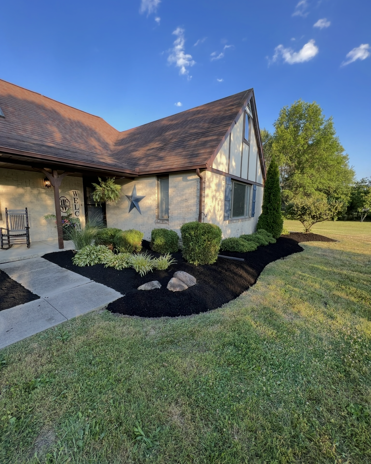 House with dark mulch beds, green bushes, and grassy lawn under a blue sky.