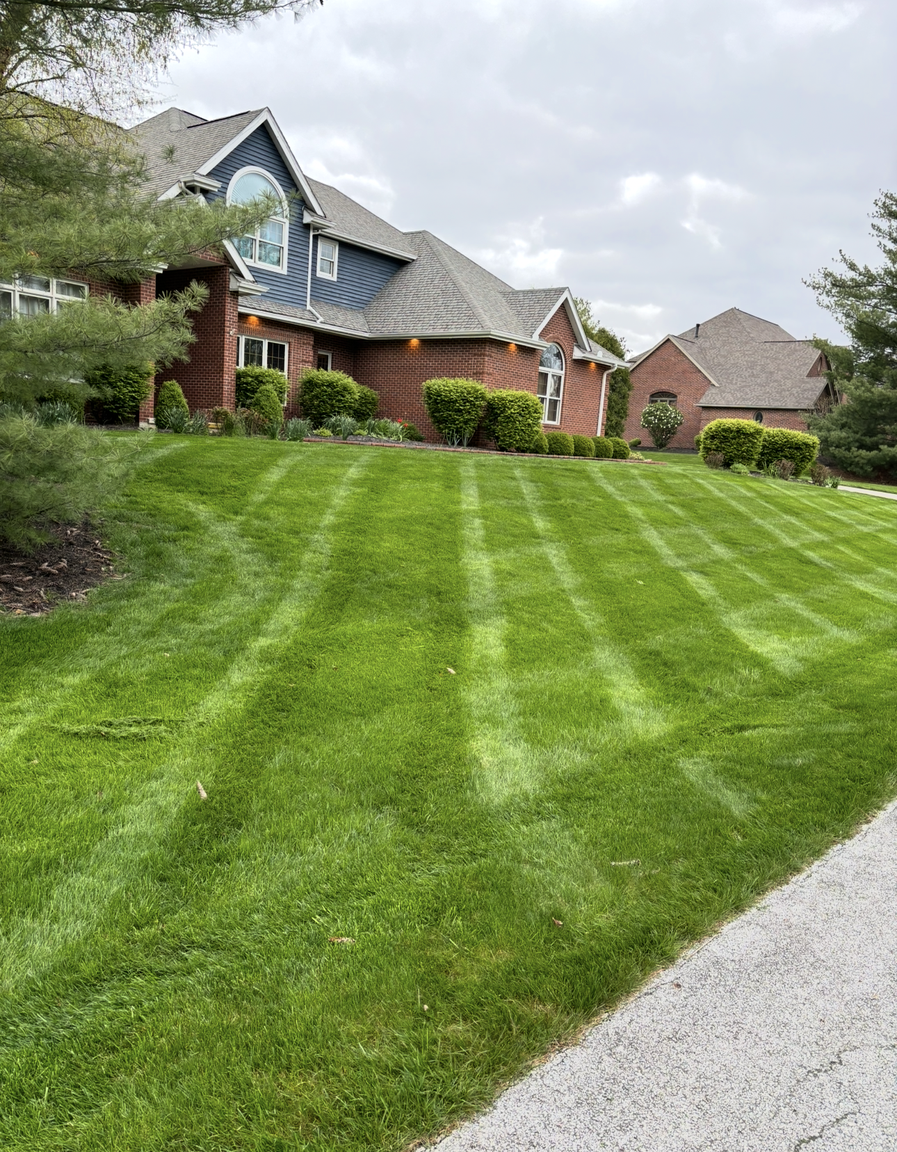Well-mowed lawn with stripes in front of a two-story house with blue siding and brick facade.