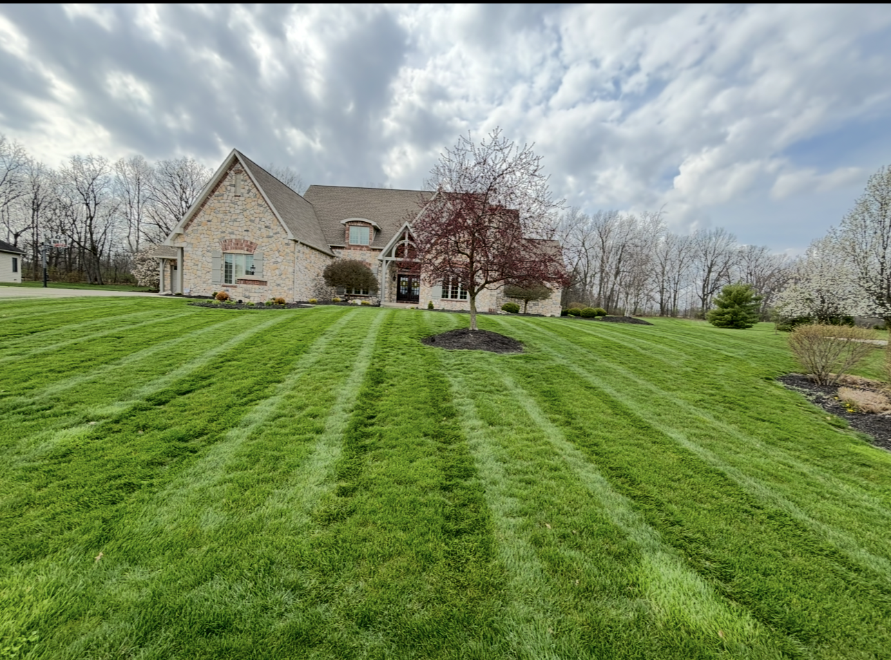 A brick house on a grassy hill with striped lawn under a cloudy sky.