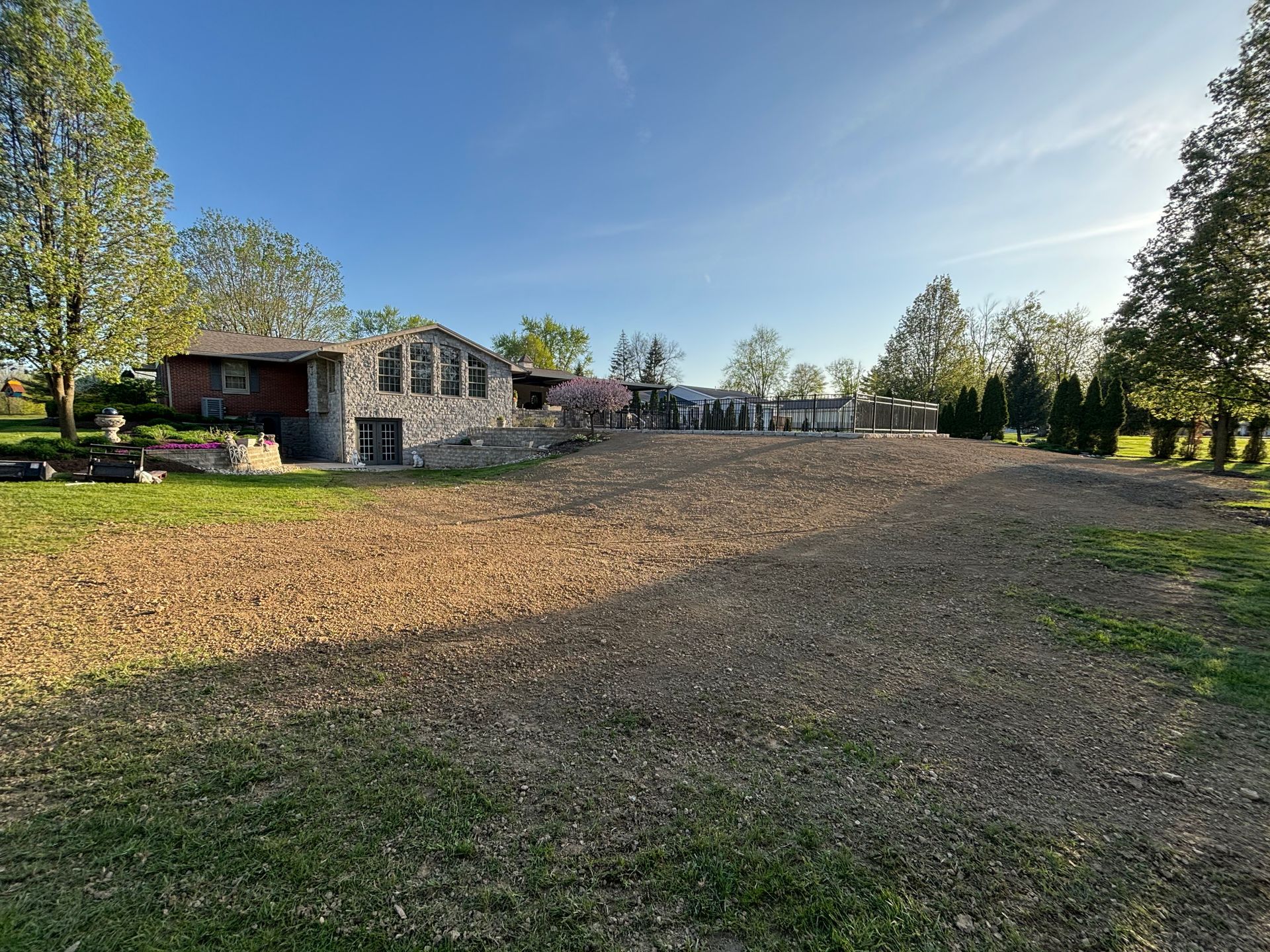 Stone building with a newly graded plot of earth in front, green grass on either side, under a clear blue sky.