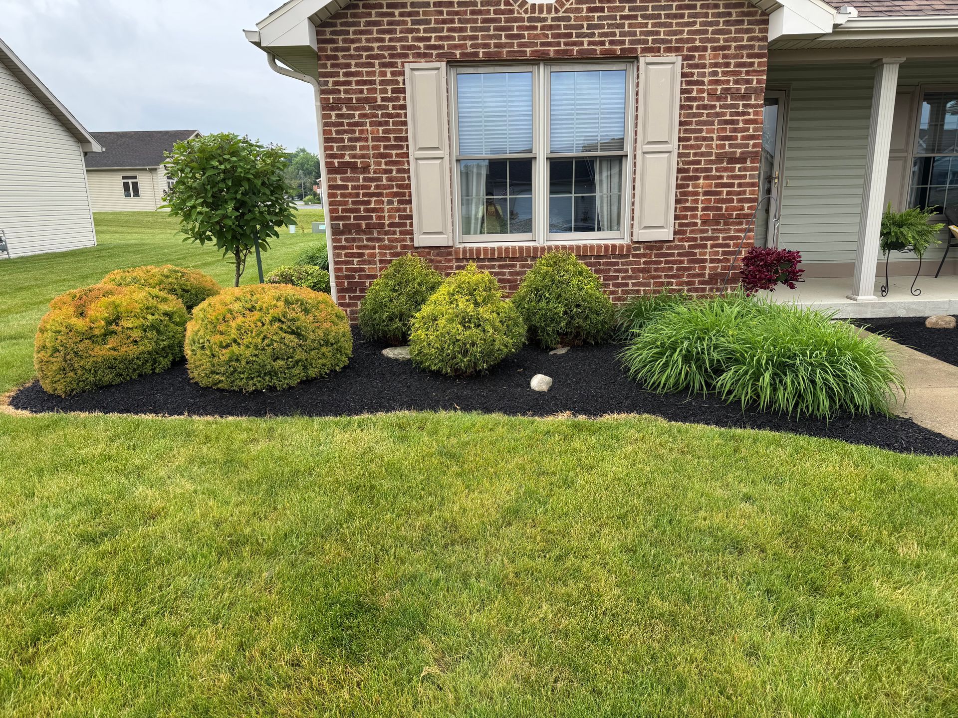 Well-manicured front yard with lawn, flower beds, and a brick house.