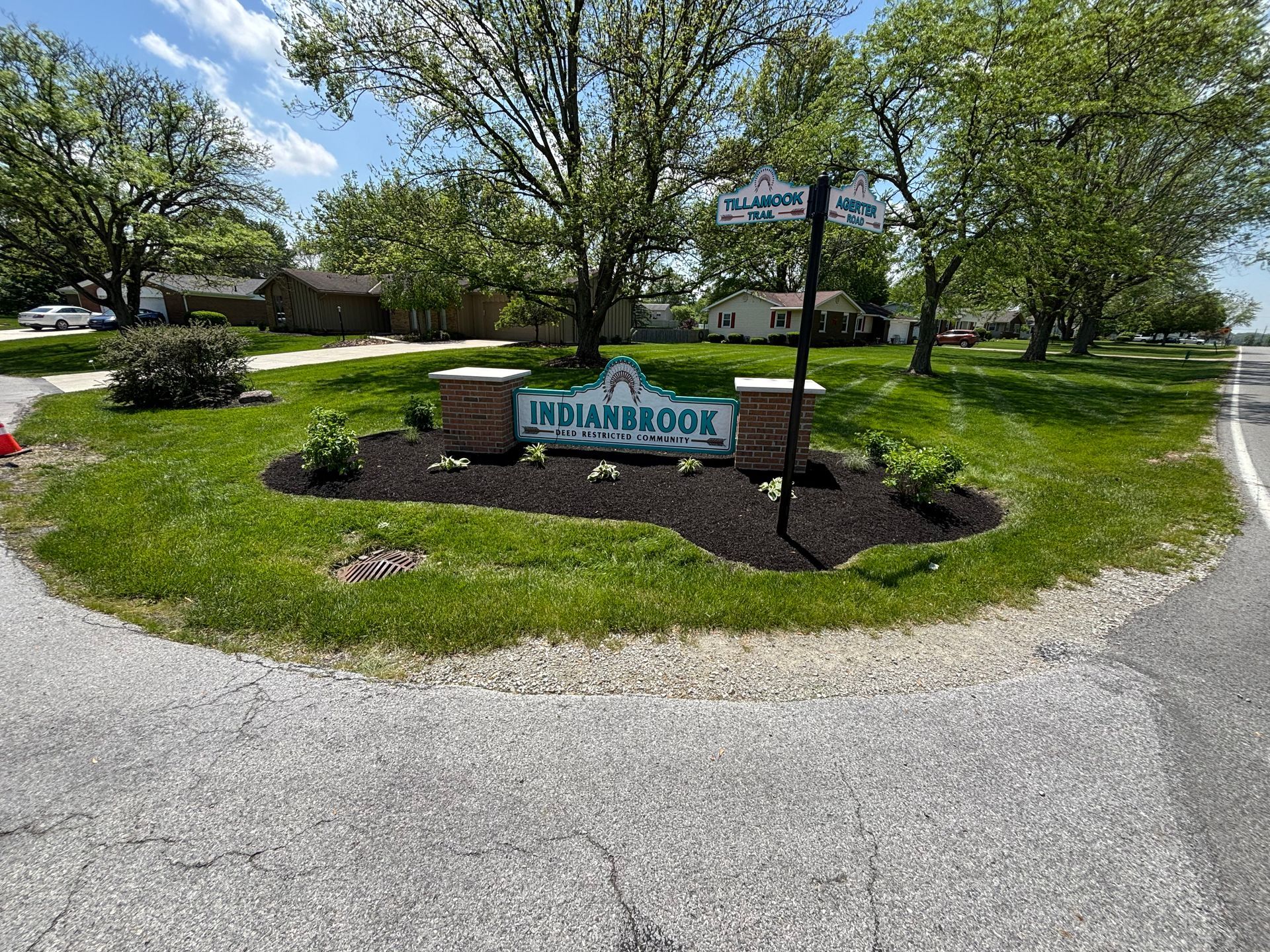 Sign for Indianbrook neighborhood with landscaped flower beds and trees at a road intersection.