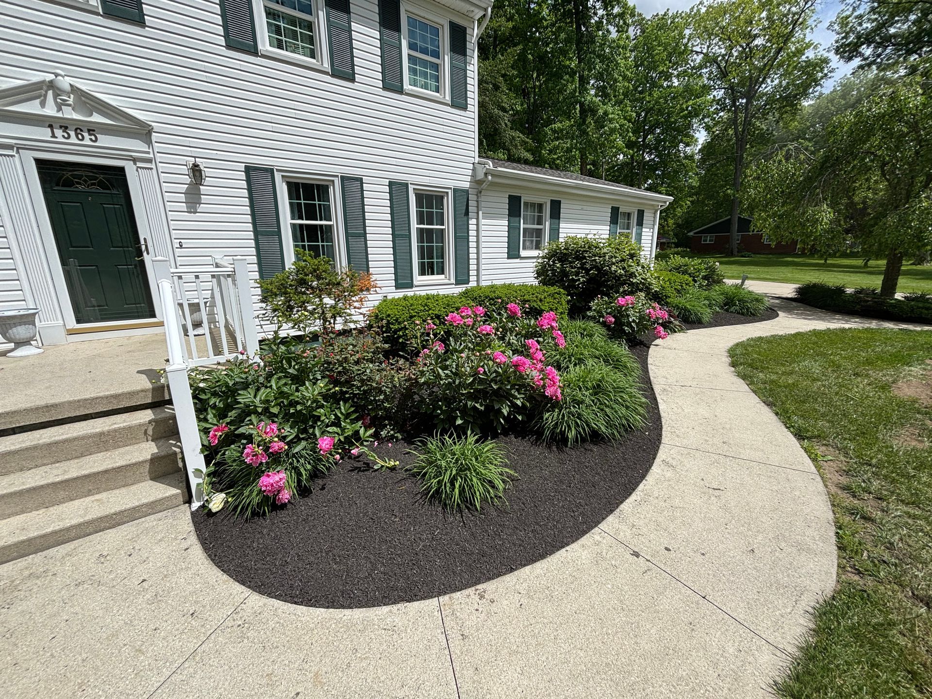 White house with a curved walkway, flower beds with pink flowers, and dark mulch.
