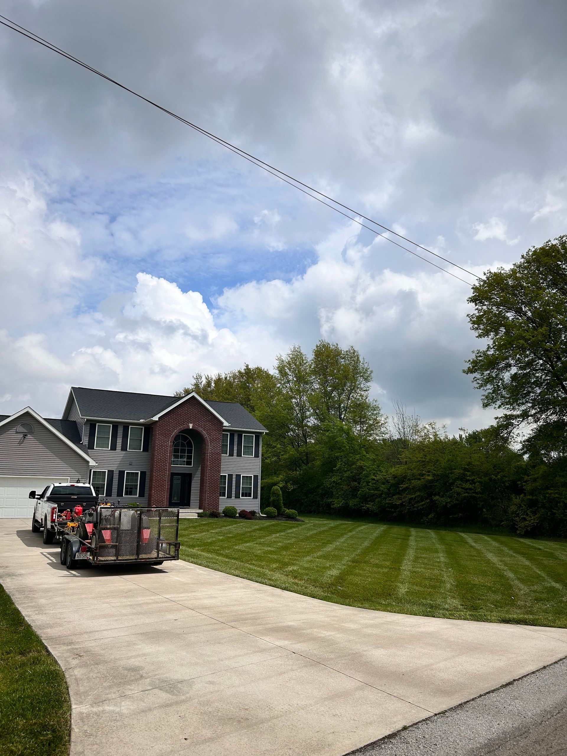 Large house with black shutters, gray siding, and a trailer on the driveway with a freshly mowed lawn.