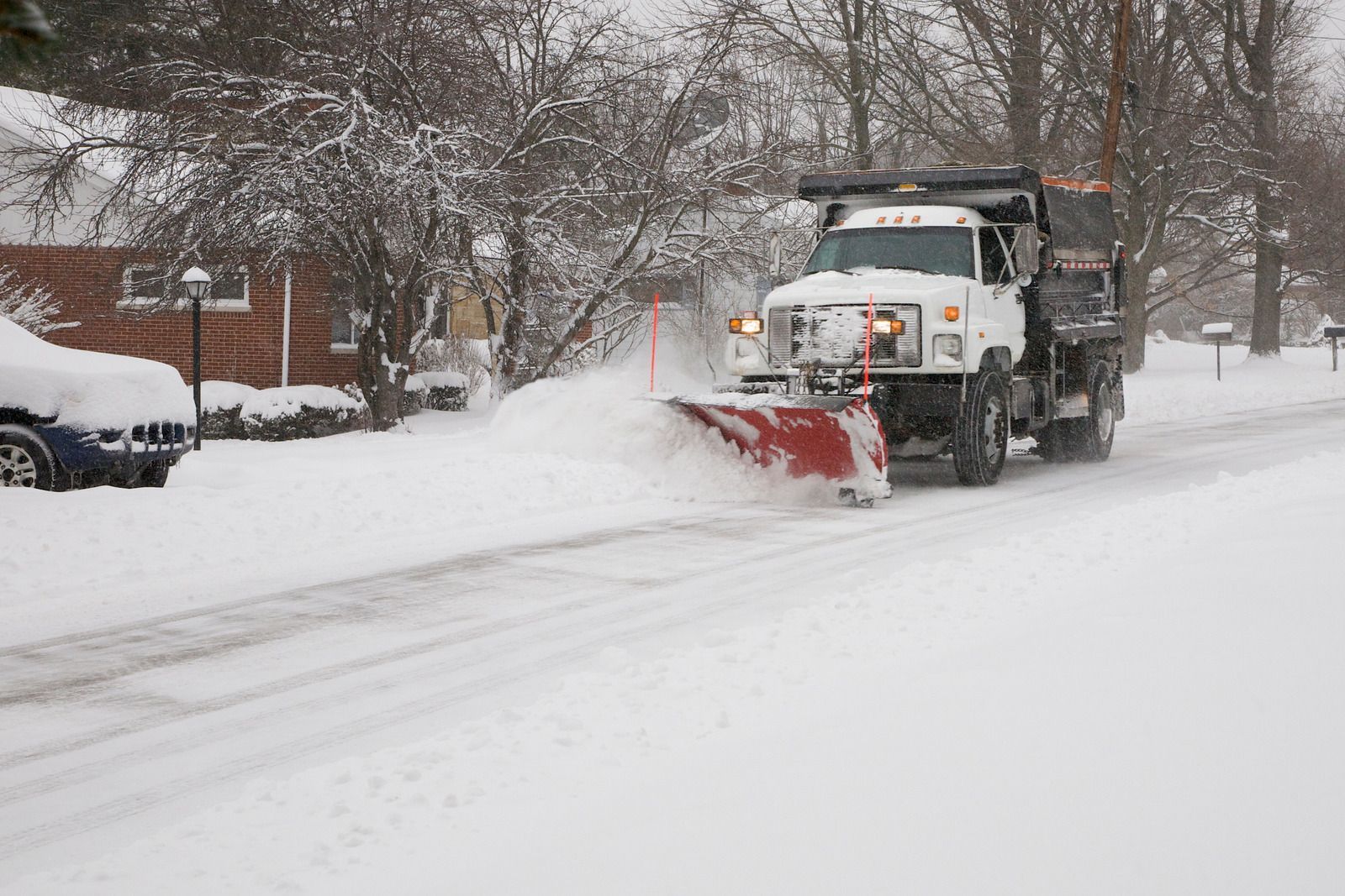 Snowplow clearing a snow-covered street in a residential area.