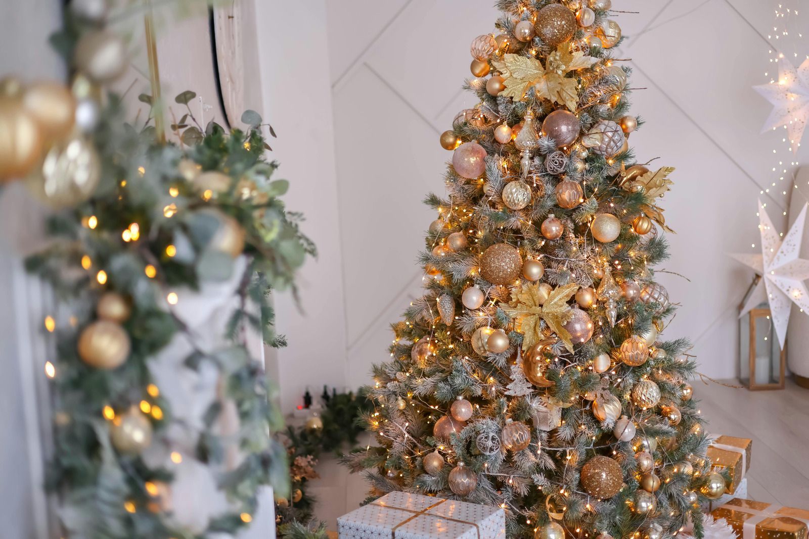 Christmas tree decorated with gold ornaments and lights, next to a smaller, similarly decorated arrangement.