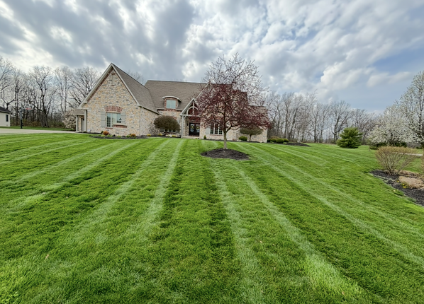 Lush green lawn with striped mowing pattern leading to a large stone house under a cloudy sky.