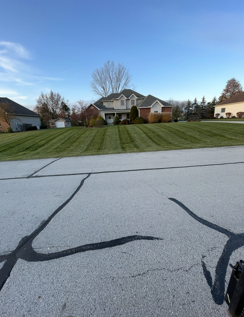 Green lawn with geometric mowing patterns, a pond in the background, and a sunny sky. Logo in the bottom right corner.
