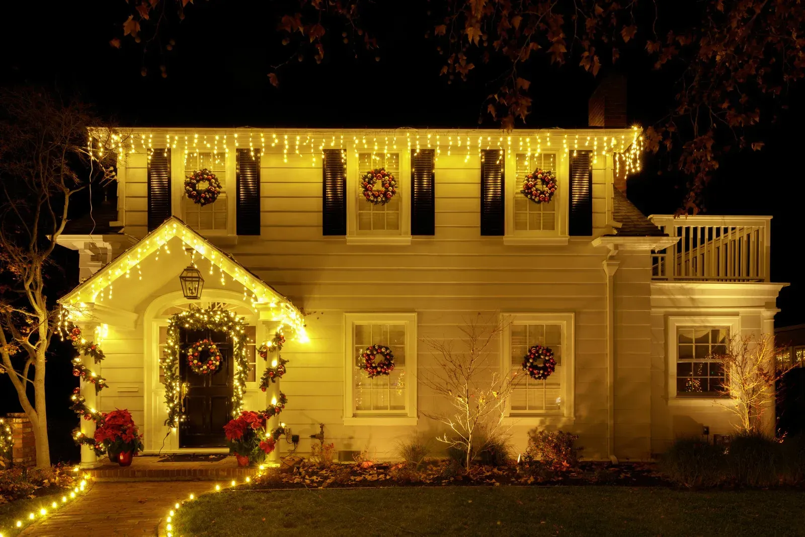 A house decorated with Christmas lights, including wreaths and string lights. It's nighttime, and the house glows.