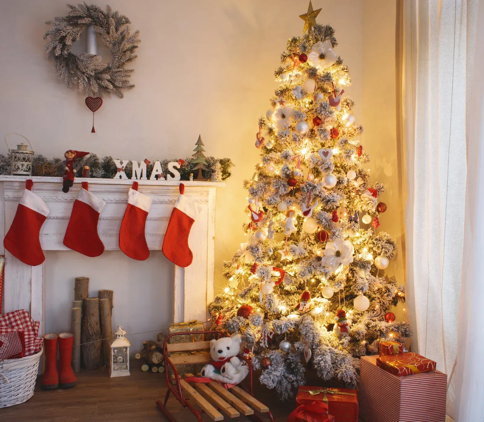 Christmas scene: snow-covered tree, fireplace with stockings, wreath, and gifts on a wooden floor.