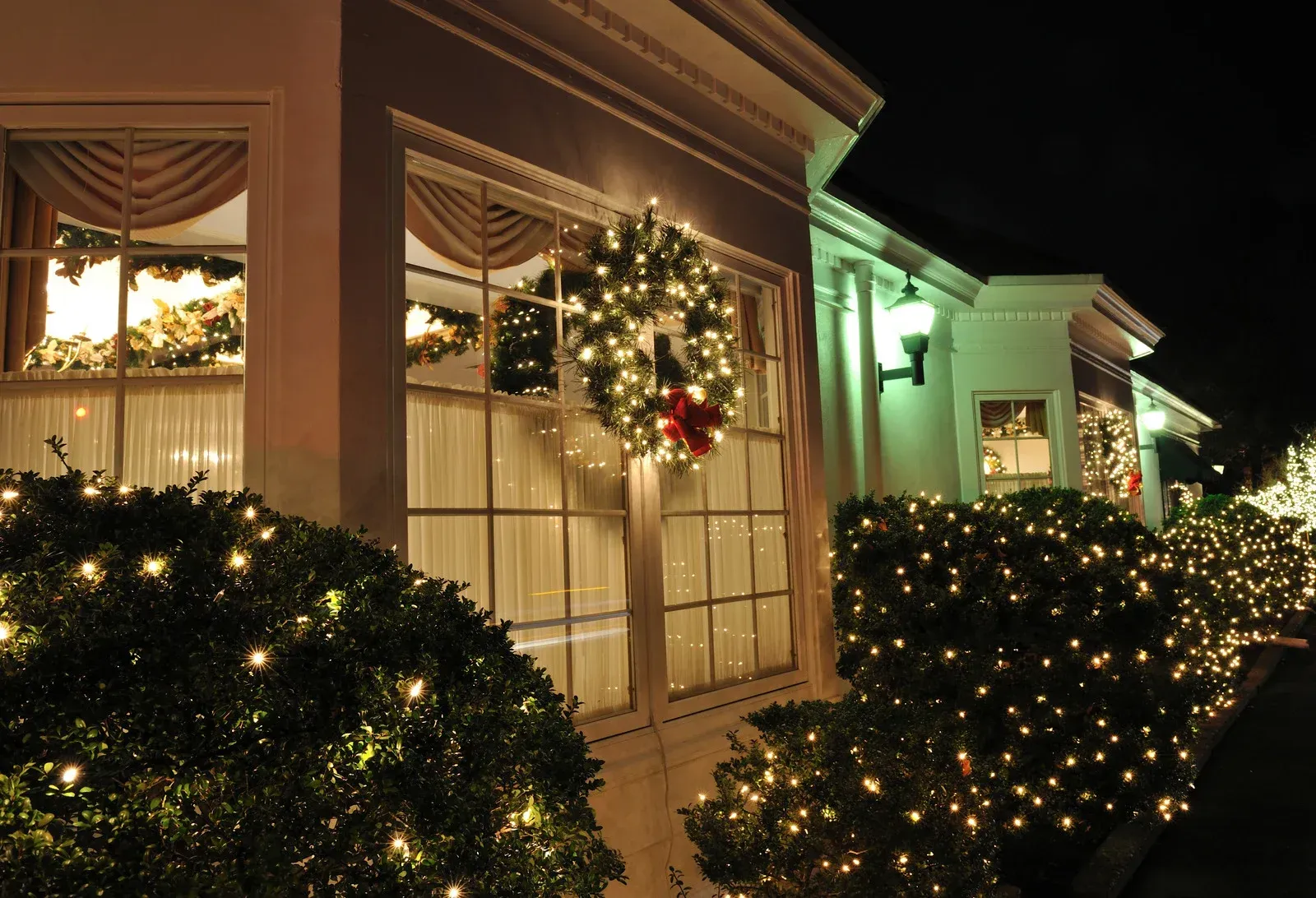 House decorated for Christmas, with string lights, a wreath, and lighted bushes.