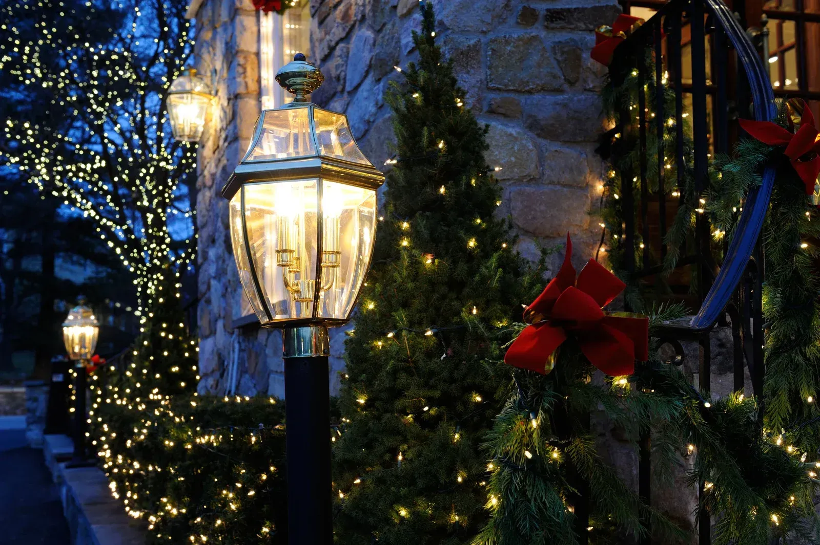 Lit Christmas decorations on a building at night, including string lights, wreaths, and a lamp post.