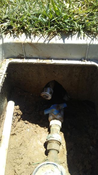 A water meter is sitting in the dirt next to a concrete box.