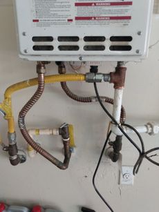 A gas water heater is connected to a wall and has a lot of wires coming out of it.