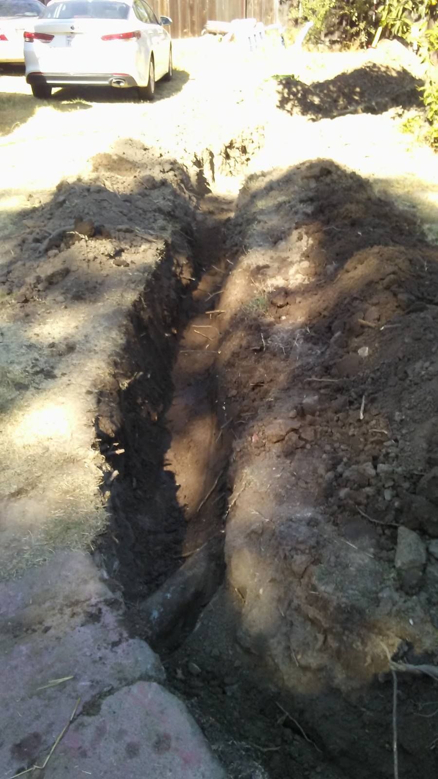 A large pile of dirt is sitting on the side of a road next to a car.
