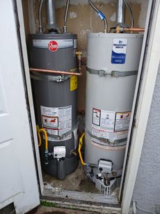 Two water heaters are stacked on top of each other in a closet.