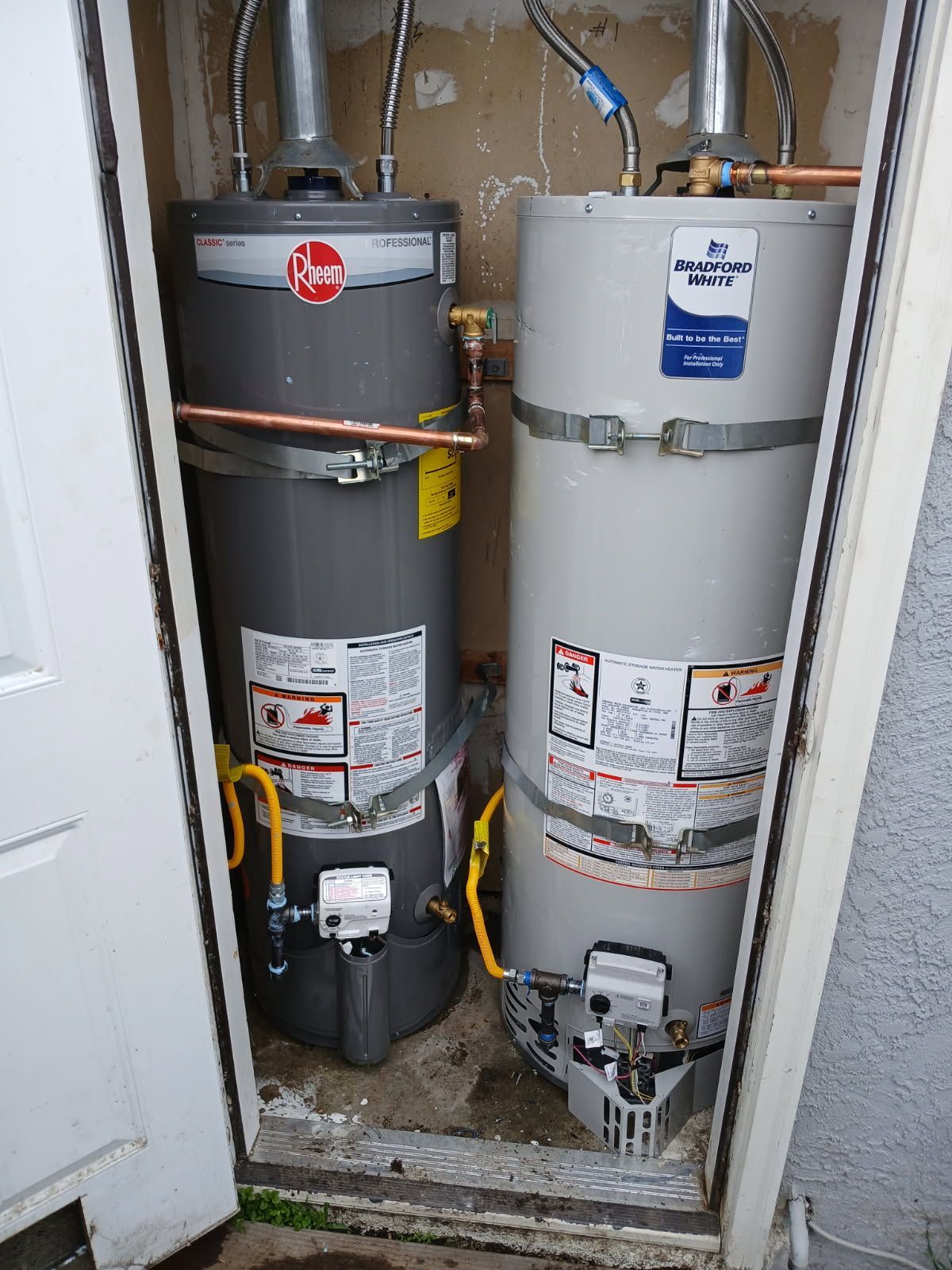 Two water heaters are stacked on top of each other in a closet.