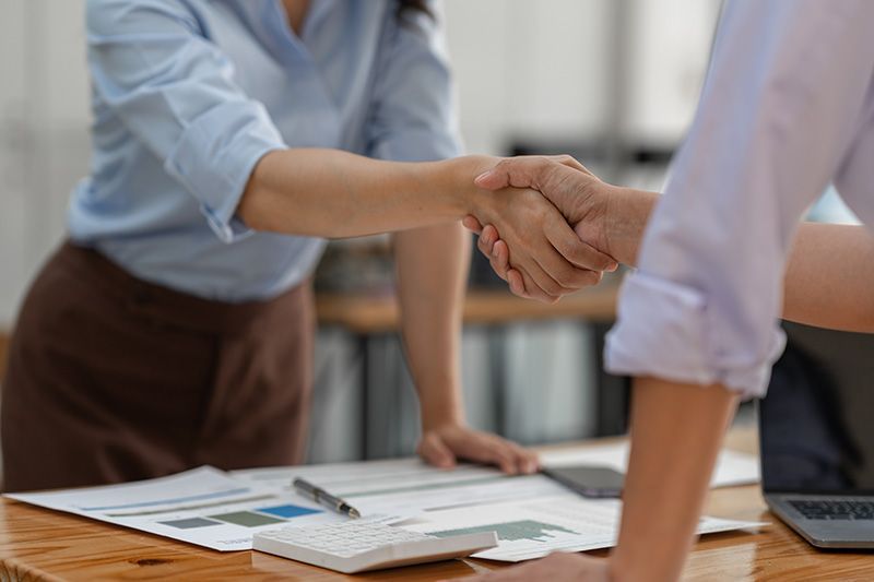 A man and a woman are shaking hands over a table.